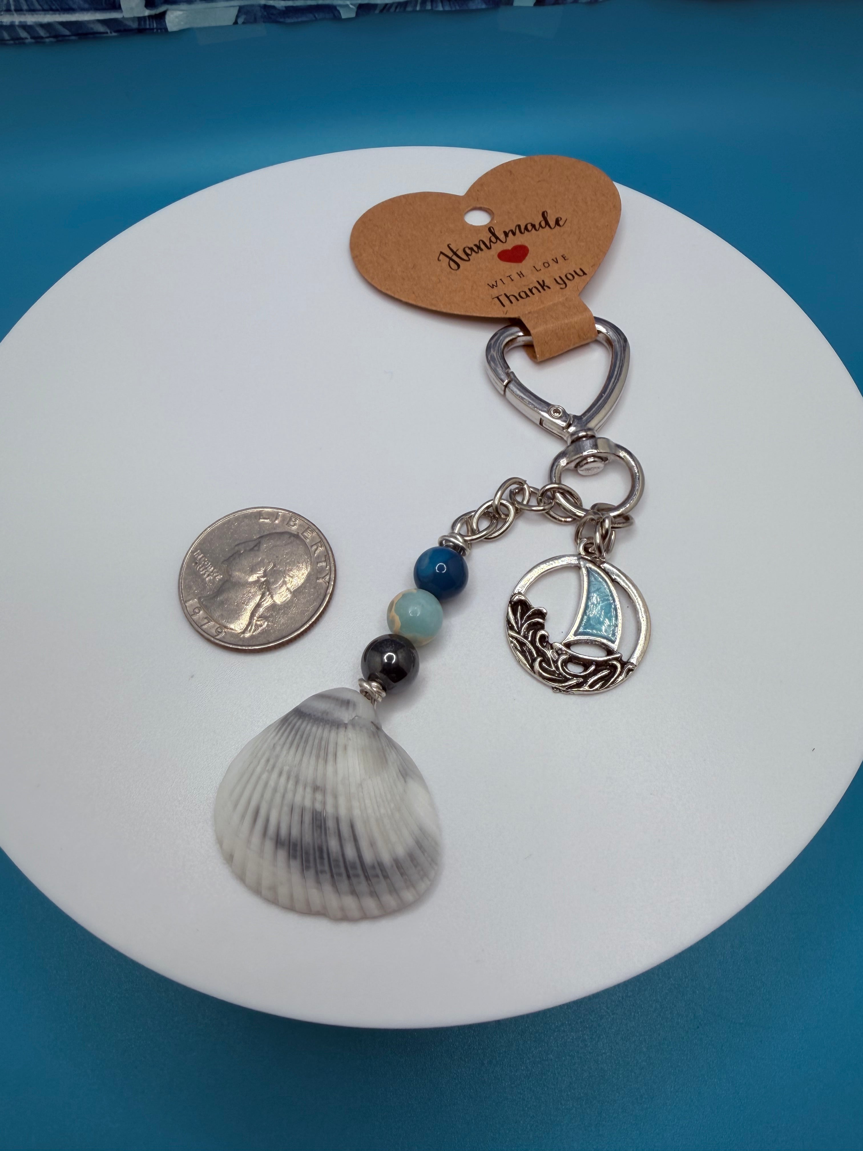Coastal sailboat scallop shell bag charm on white structured handbag with blue shell print background