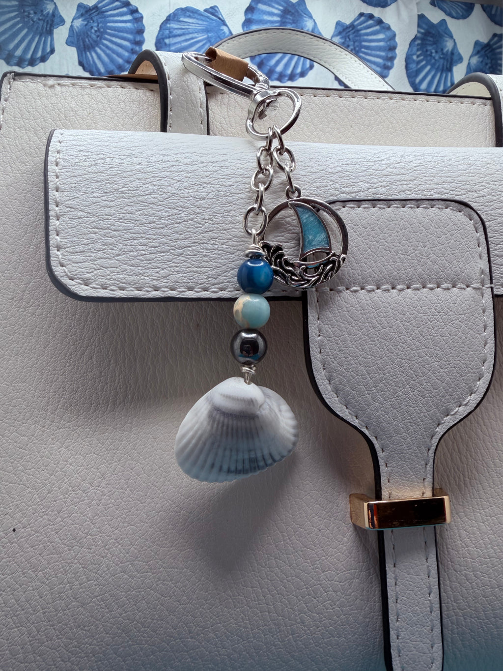 Coastal sailboat scallop shell bag charm with quarter for scale on blue background