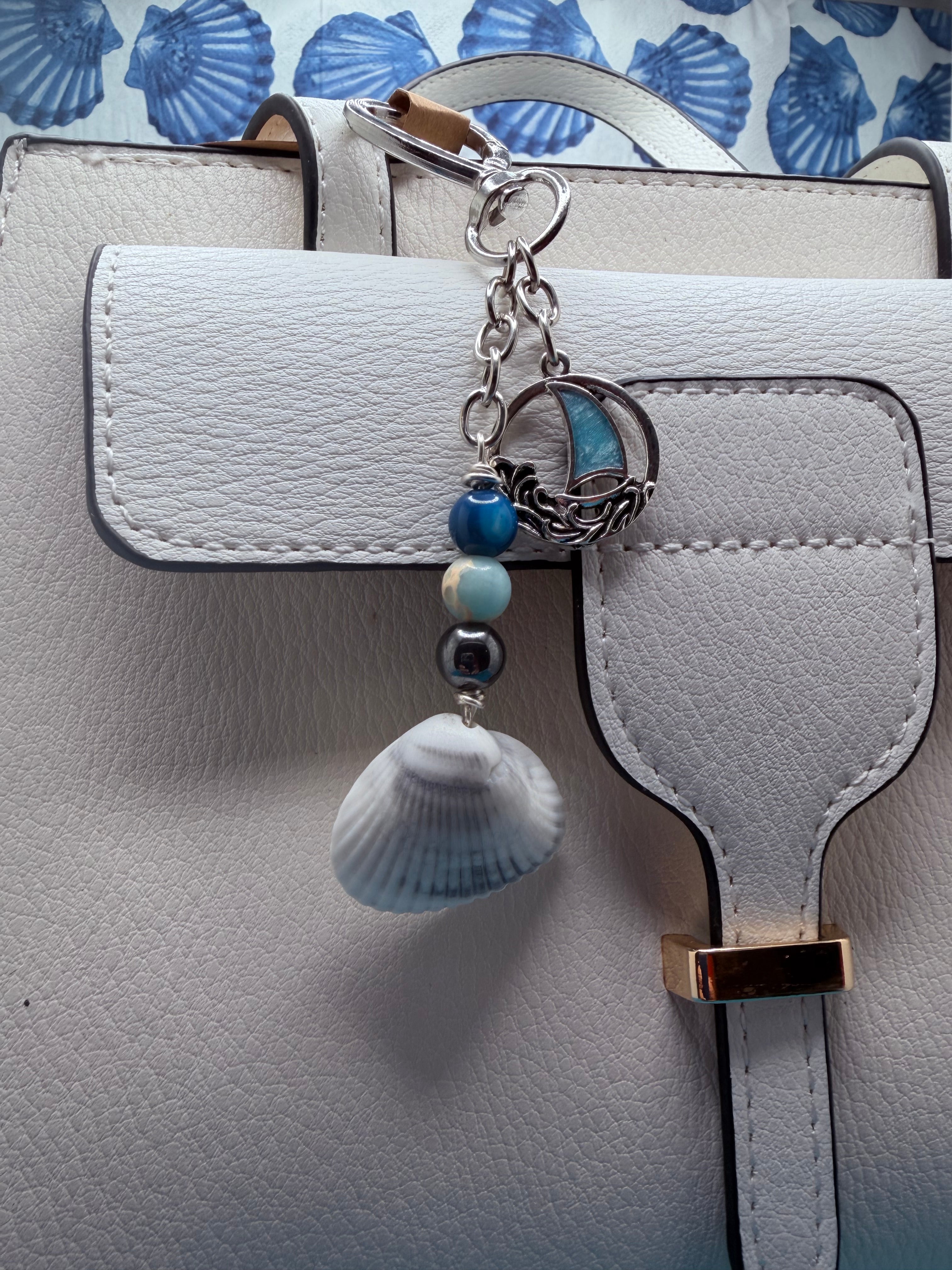 Coastal sailboat scallop shell bag charm with quarter for scale on blue background