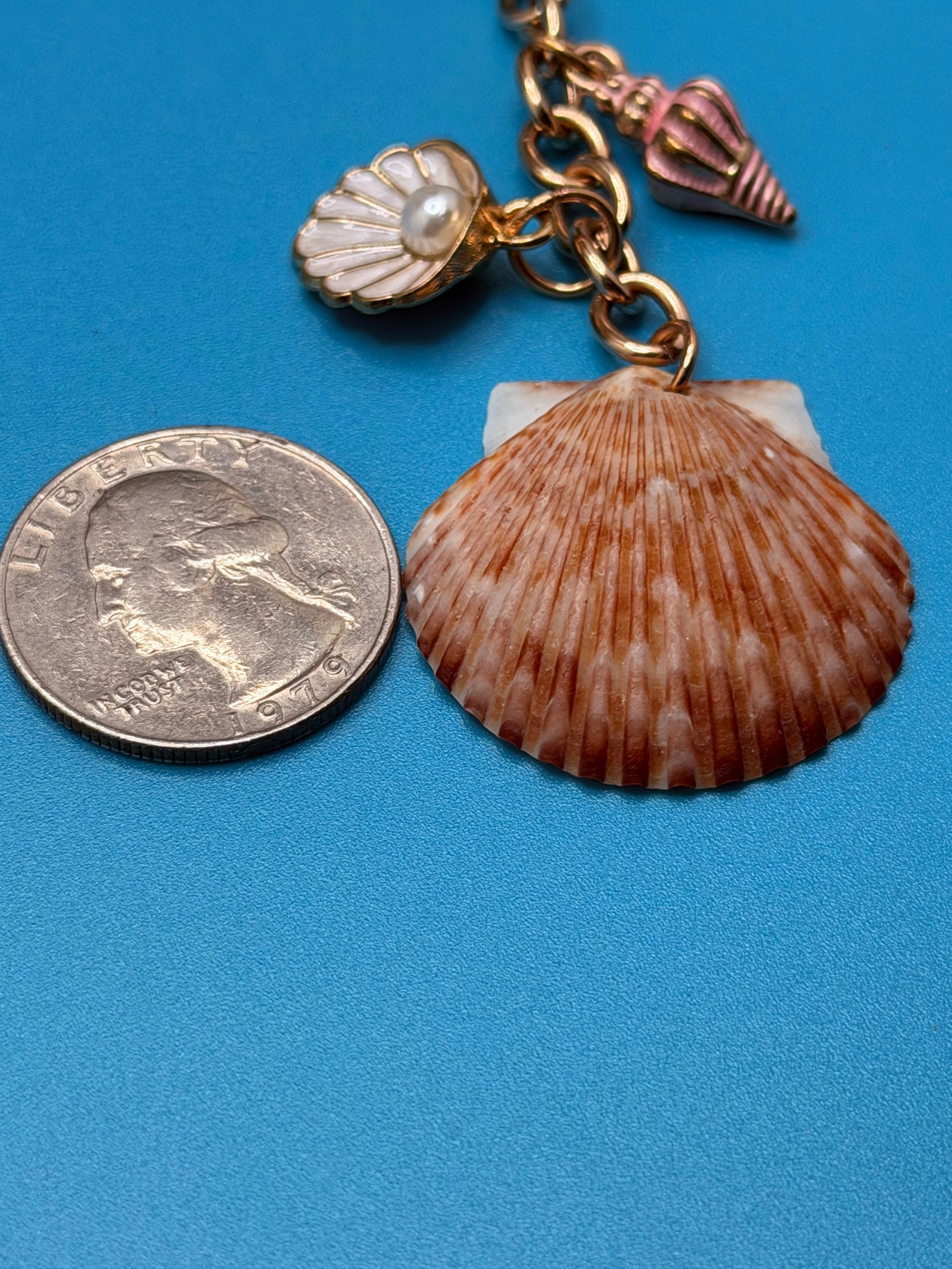 Close-up of chocolate seashell bag charm showing scallop shell and pearl shell charm detail with quarter for scale