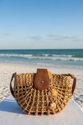 Chocolate seashell bag charm full view on woven straw bag with shell print background