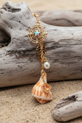 Celestial Shores lightning whelk shell bag charm styled on woven straw bag showing compass star charm