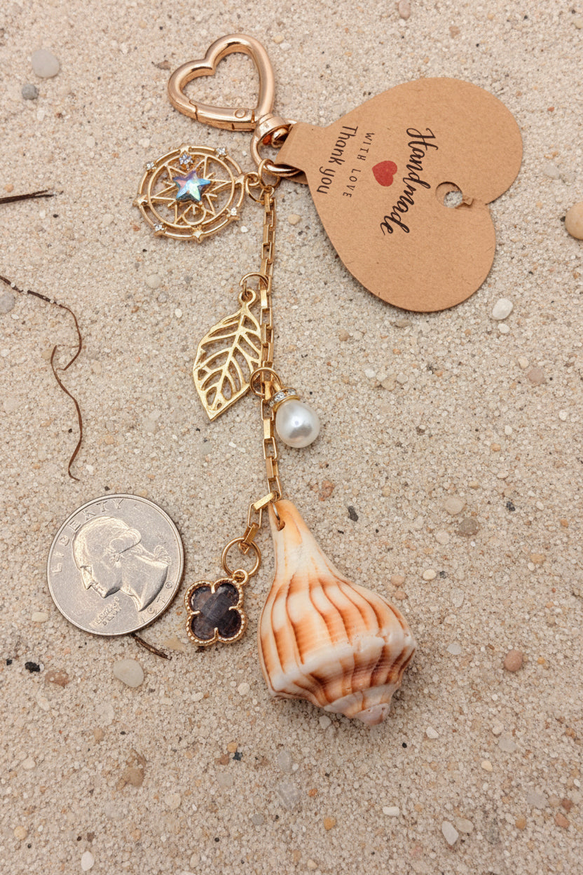 Celestial Shores lightning whelk shell bag charm full view on blue background with quarter for scale showing heart carabiner clasp