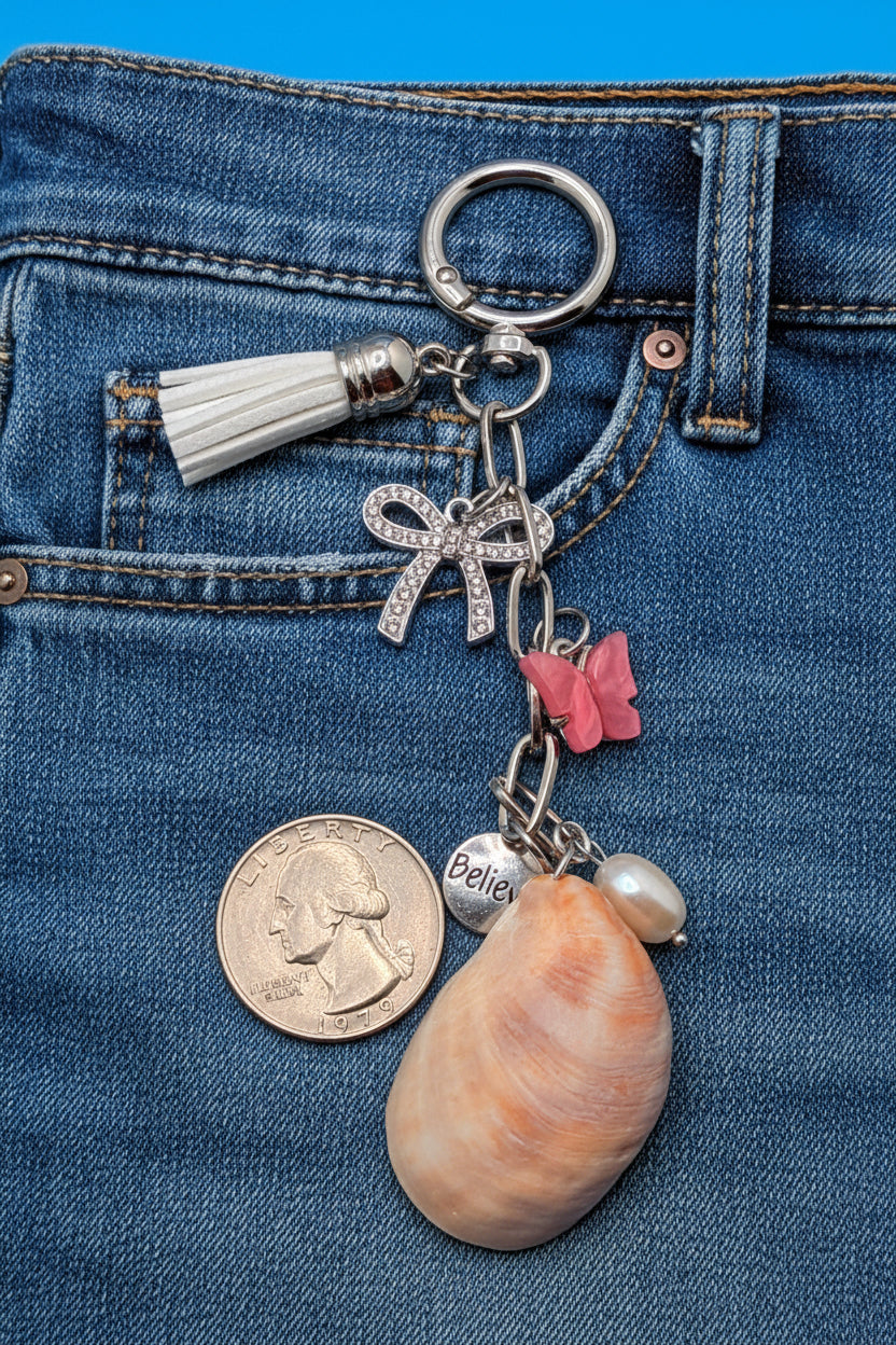 Believe and Bloom slipper shell keychain with quarter for scale on blue background showing full keychain