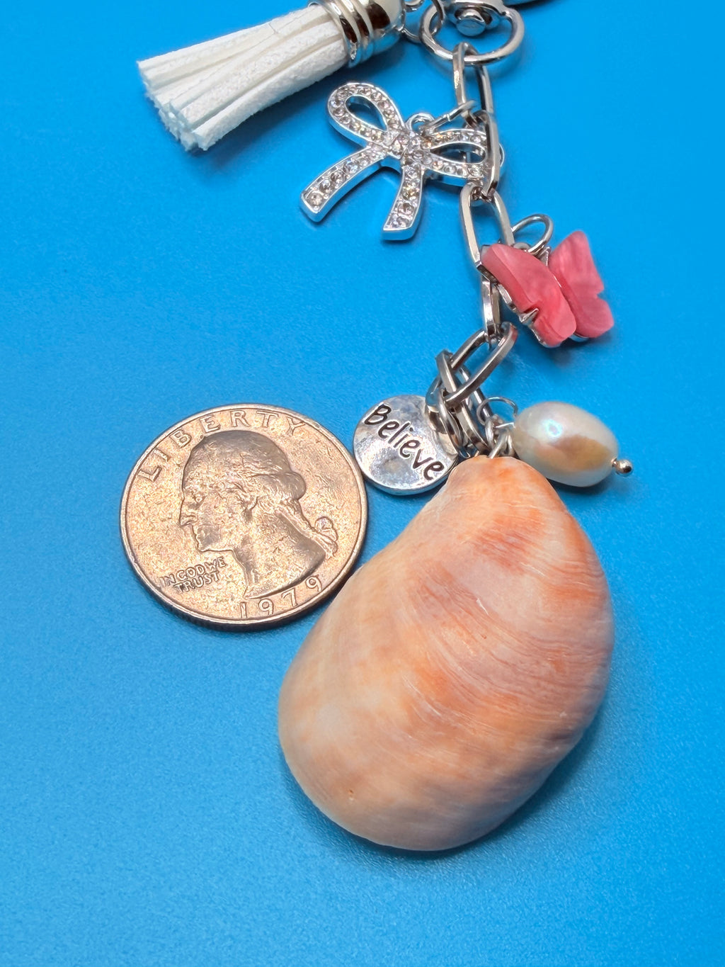 Believe and Bloom slipper shell keychain styled on woven straw tote bag with shell print background