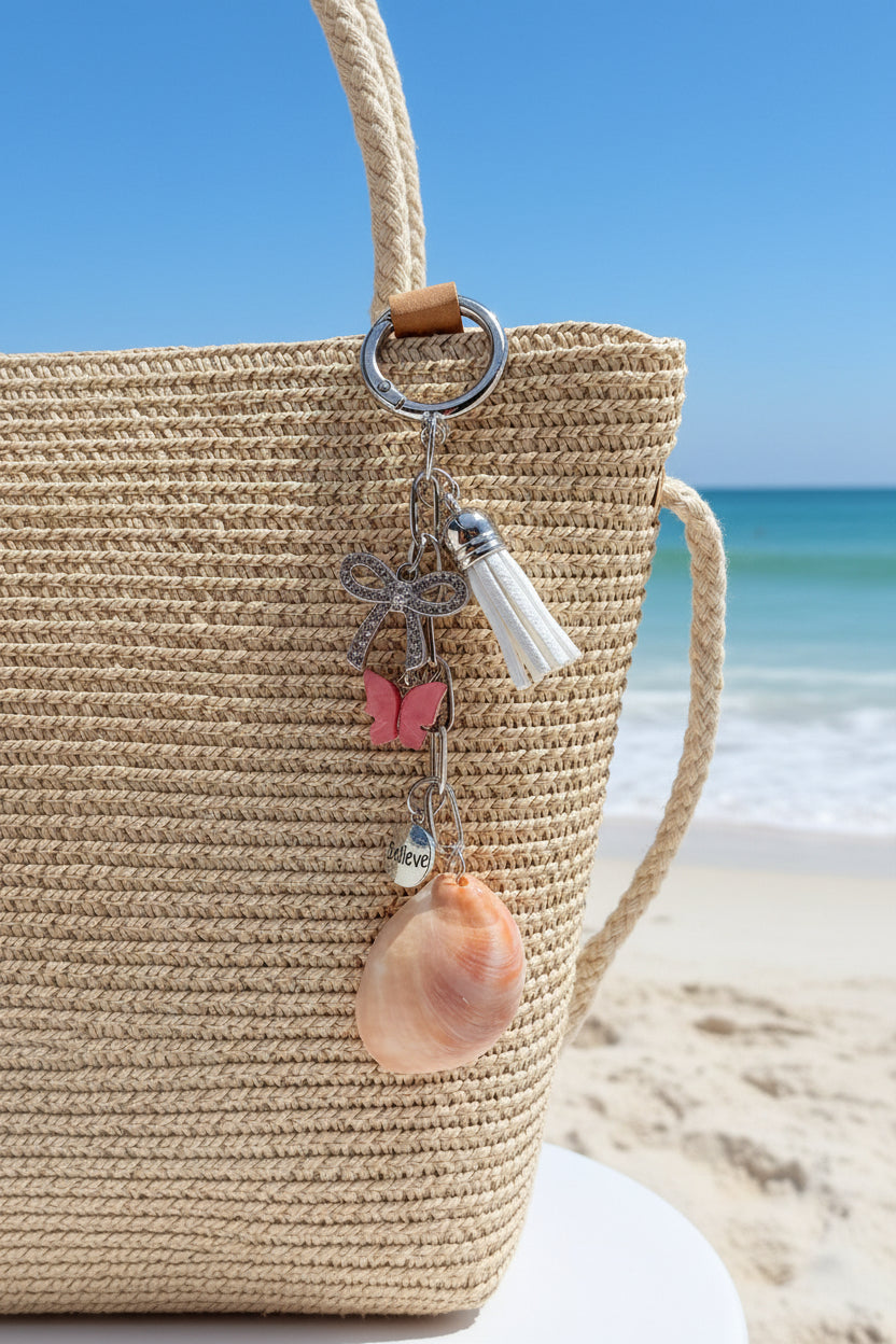 Believe and Bloom slipper shell keychain on woven straw bag close-up showing bow and butterfly charms