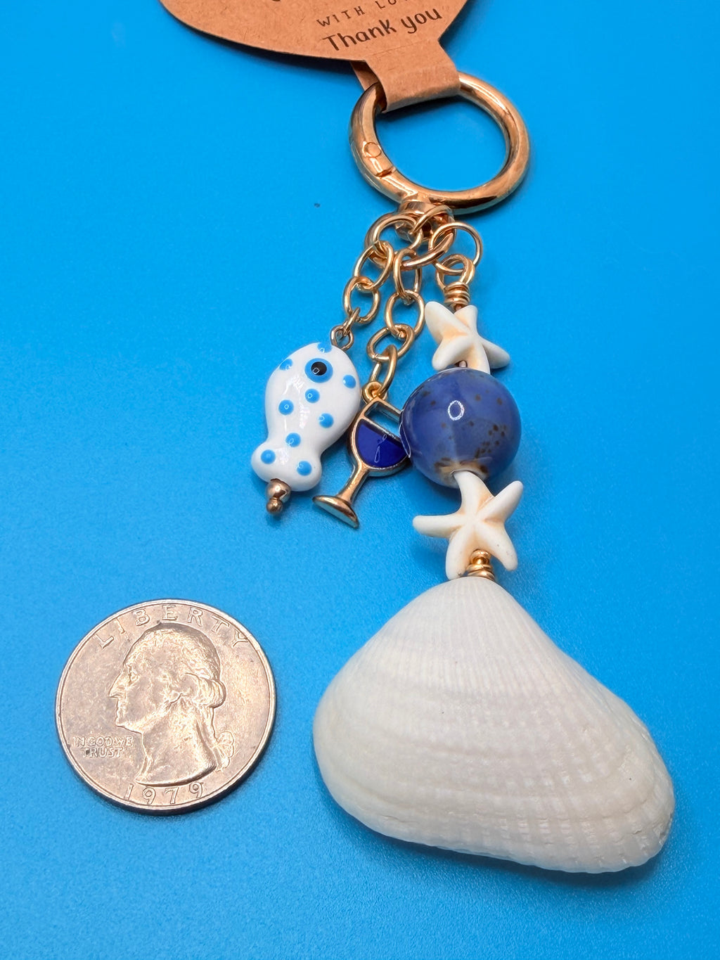 Florida ark shell bag charm close-up showing ark shell, starfish beads, periwinkle gemstone and blue enamel wine glass charm on blue background