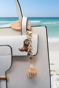 Boots and the Shore lightning whelk shell bag charm full view on blue background with quarter for scale