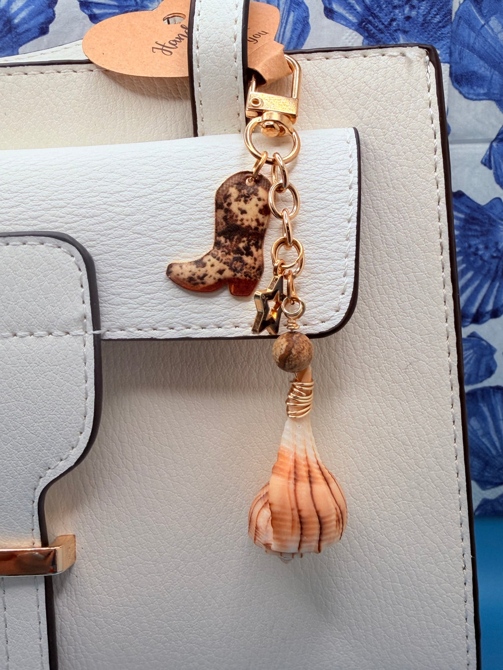 Boots and the Shore lightning whelk shell bag charm close-up showing wire wrap and natural stone bead on blue background