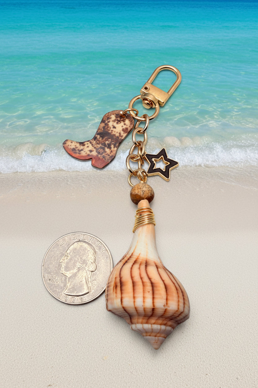 Boots and the Shore lightning whelk shell bag charm styled on white structured handbag with blue floral background