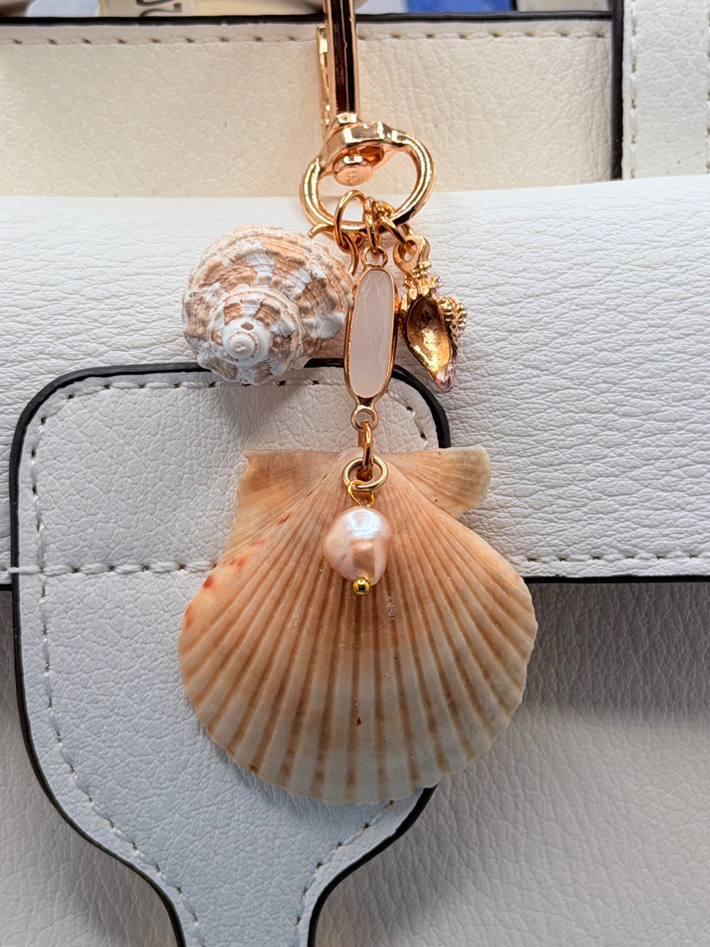 Dual Shores bag charm close-up on white leather bag showing scallop shell and pearl drop