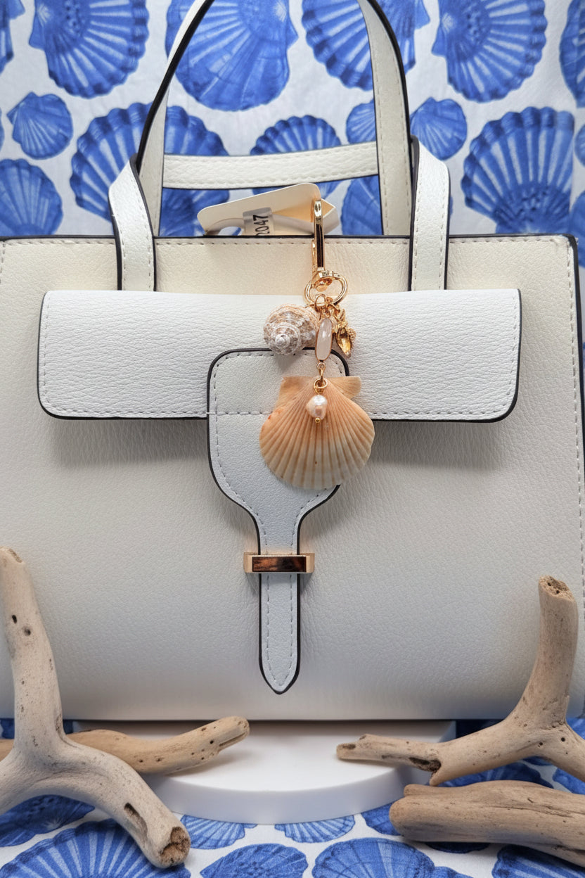 Dual Shores bag charm full view on white tote bag with coastal shell print background