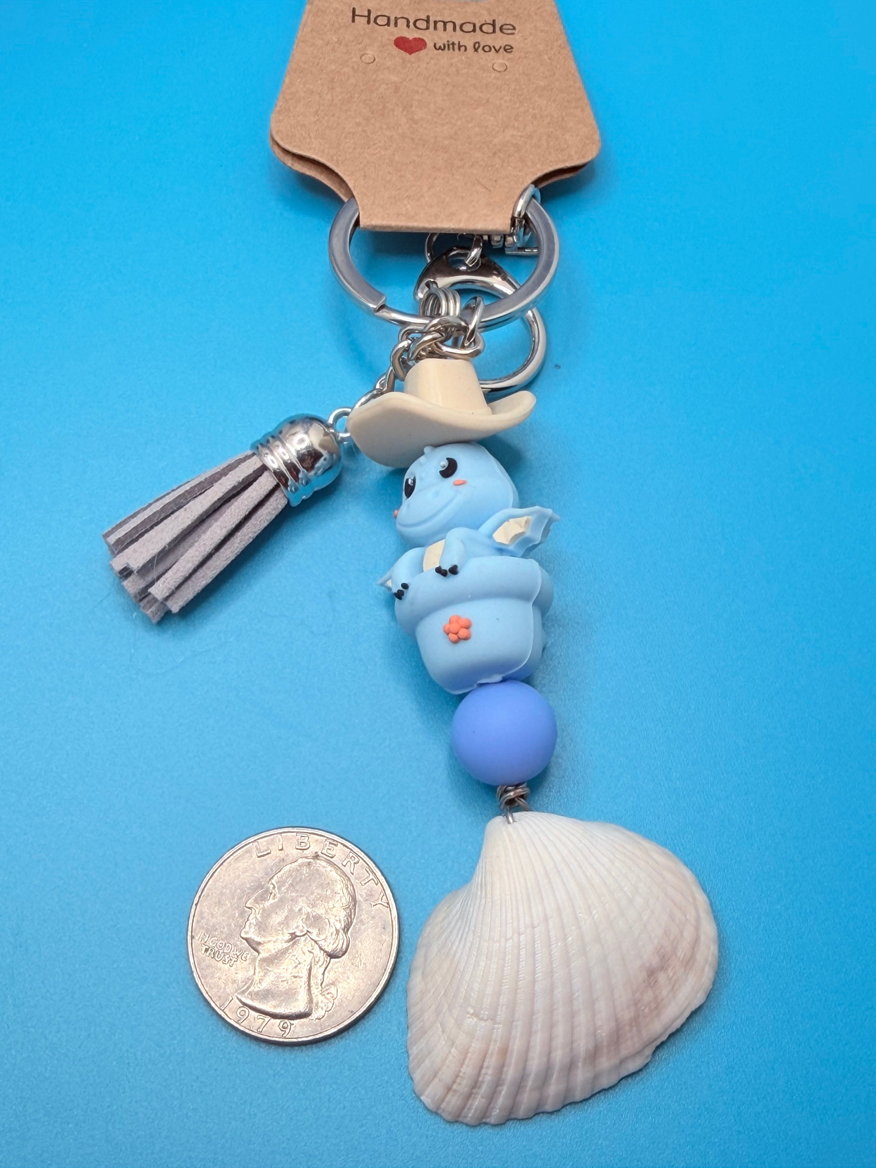 Cowboy Dragon ark shell keychain with quarter for scale on blue background showing full length