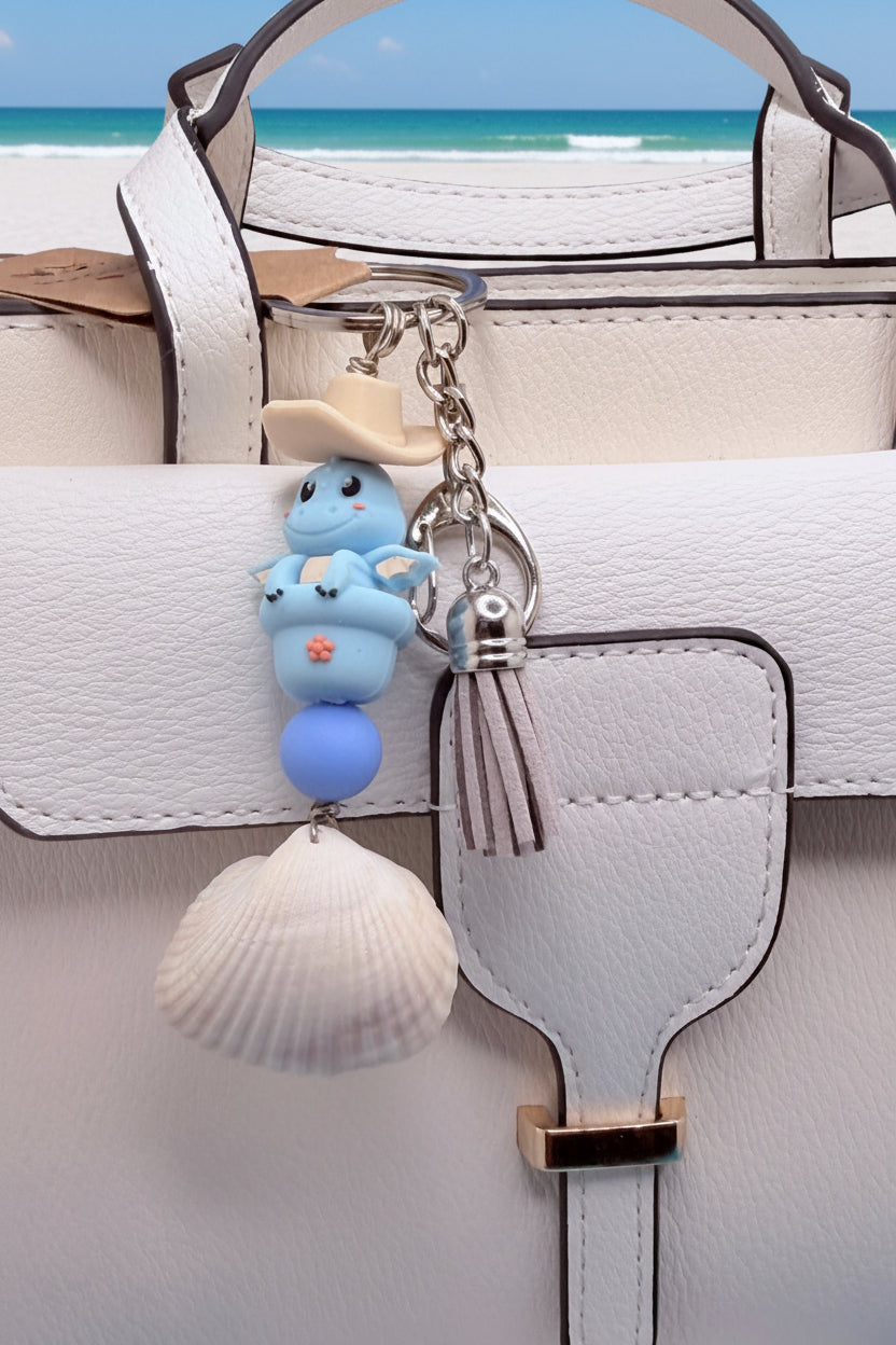Cowboy Dragon ark shell keychain on white handbag close-up showing periwinkle bead and ark shell detail
