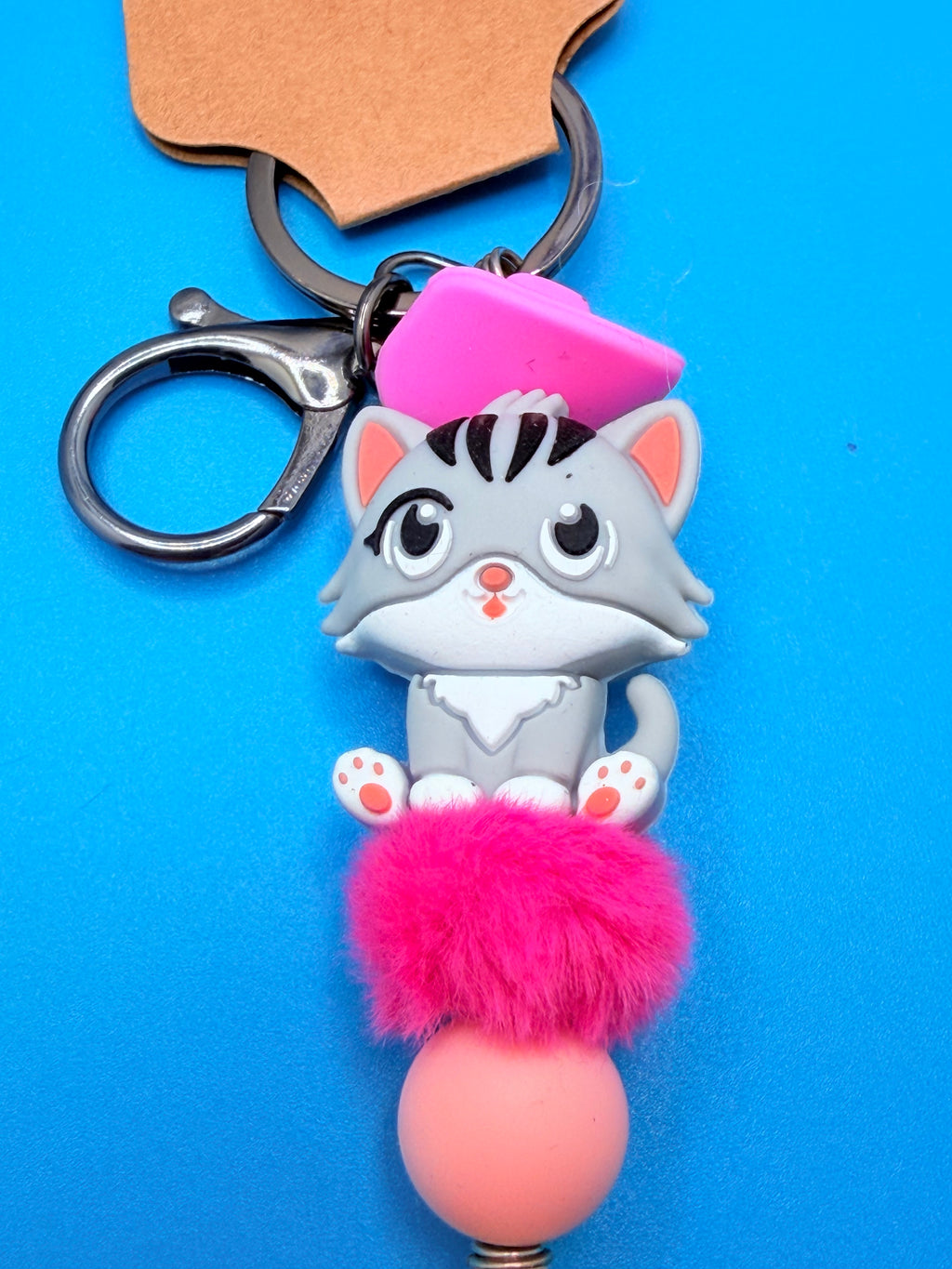 Pink Beret Cat lettered olive shell keychain with quarter for scale on blue background showing full keychain