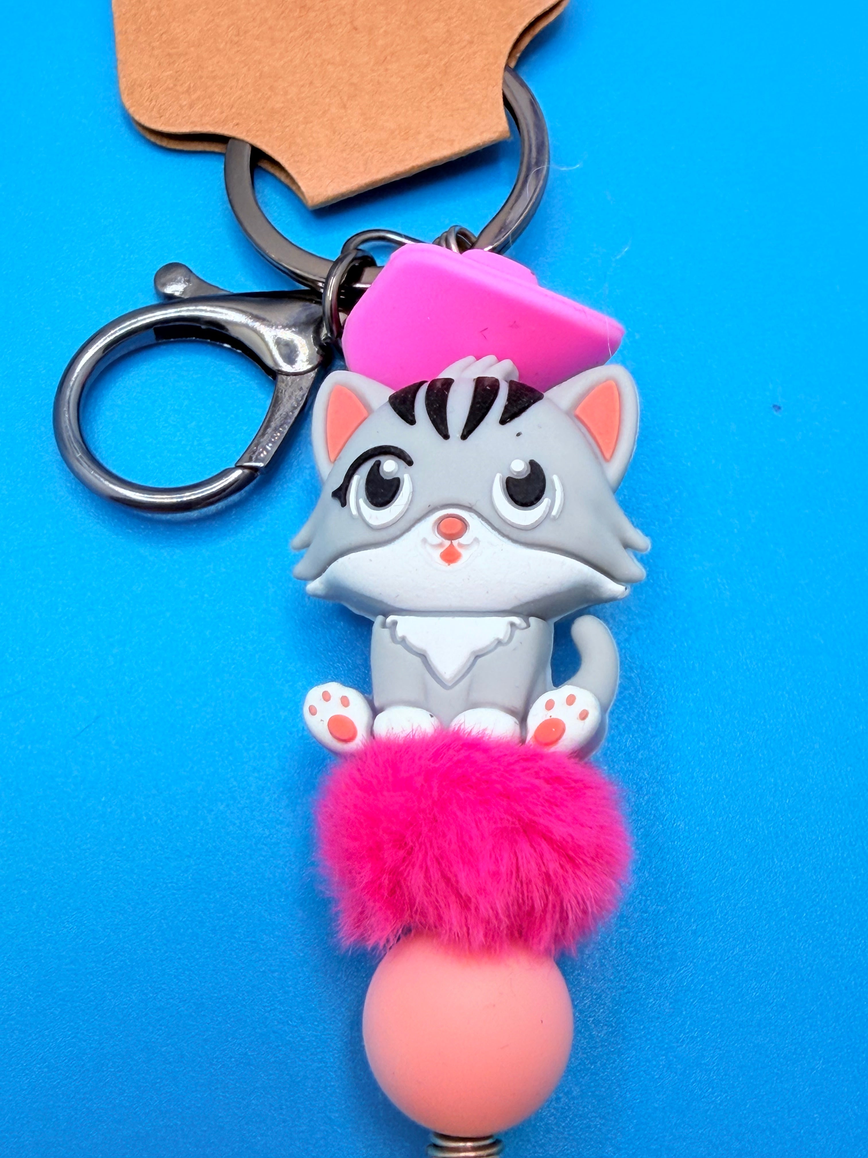 Pink Beret Cat lettered olive shell keychain with quarter for scale on blue background showing full keychain