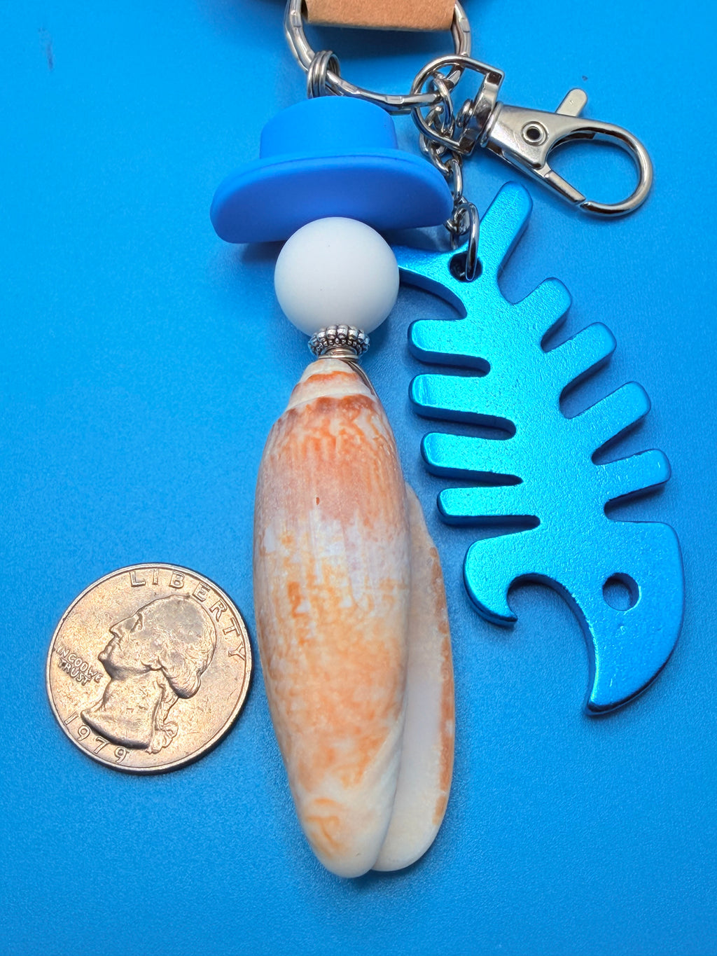 Lettered Olive fishbone bottle opener keychain on woven straw bag showing full length with blue floral background