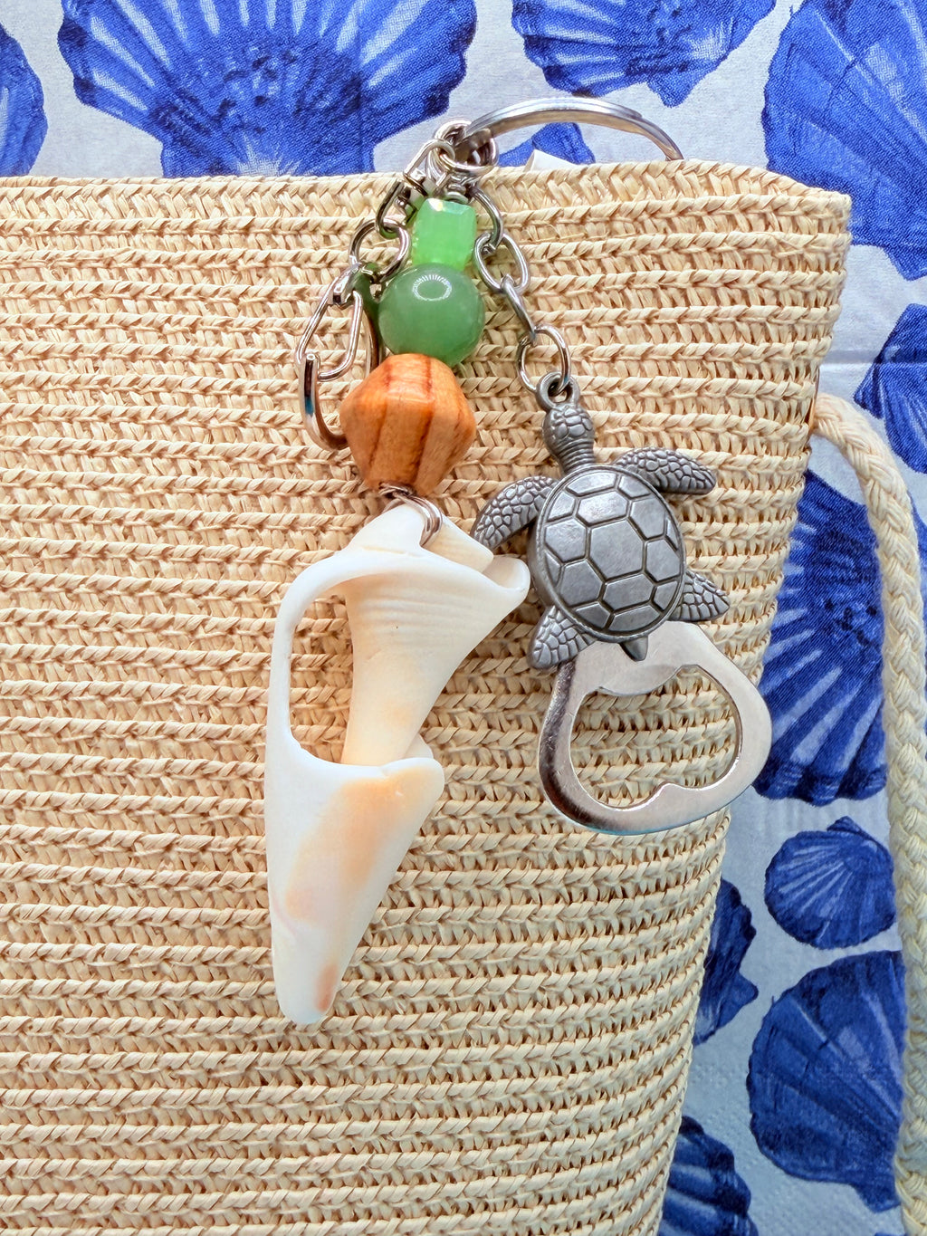 Sea Turtle conch shell bottle opener keychain on woven straw bag close-up showing conch shell fragment and green beads