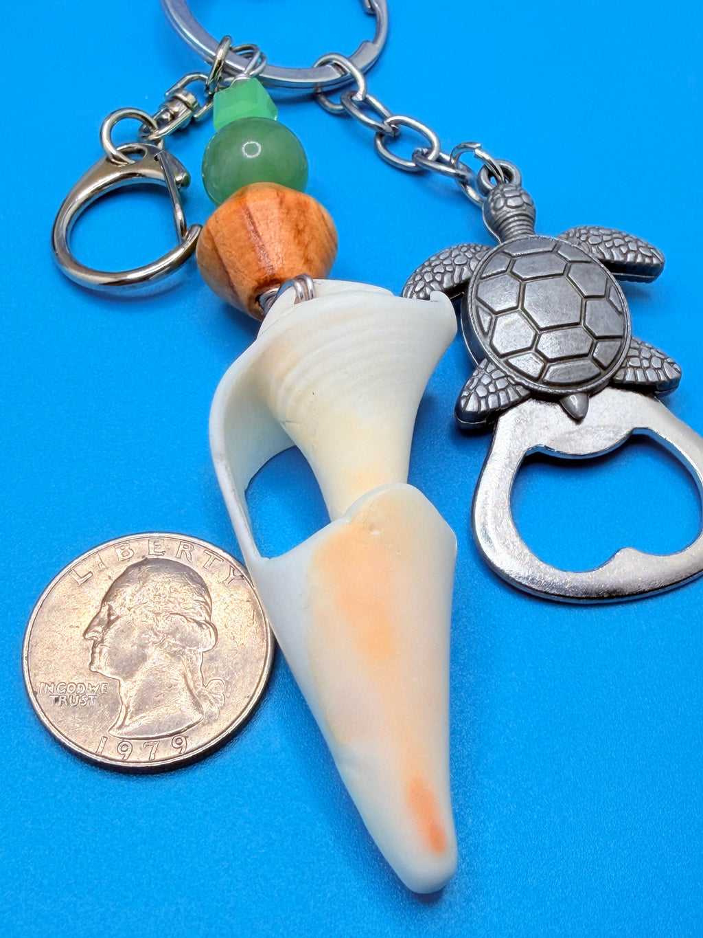 Sea Turtle conch shell bottle opener keychain with quarter for scale on blue background showing full keychain and SKU tag