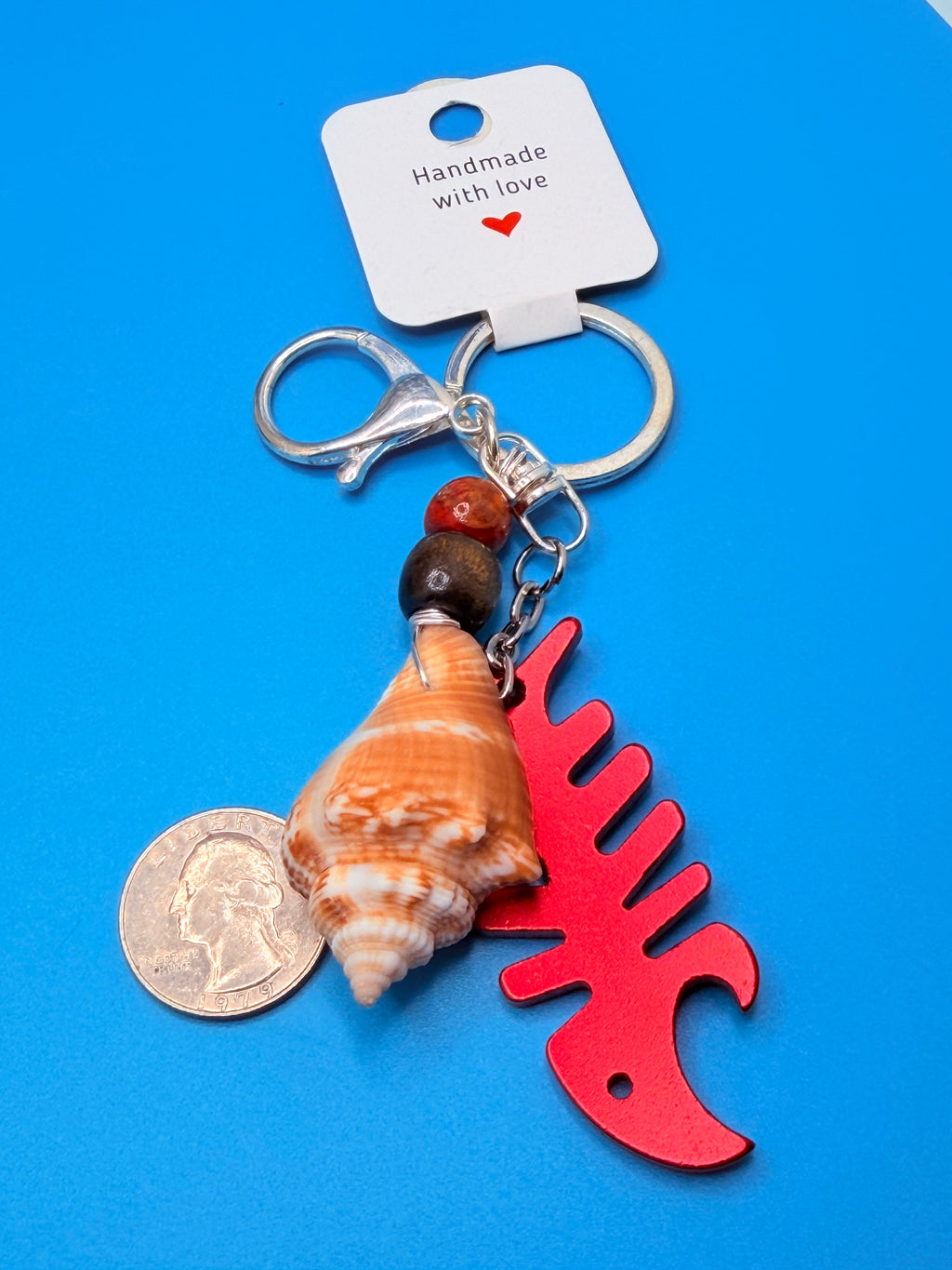 Florida conch shell red fishbone bottle opener keychain with quarter for scale on blue background showing fishbone bottle opener charm
