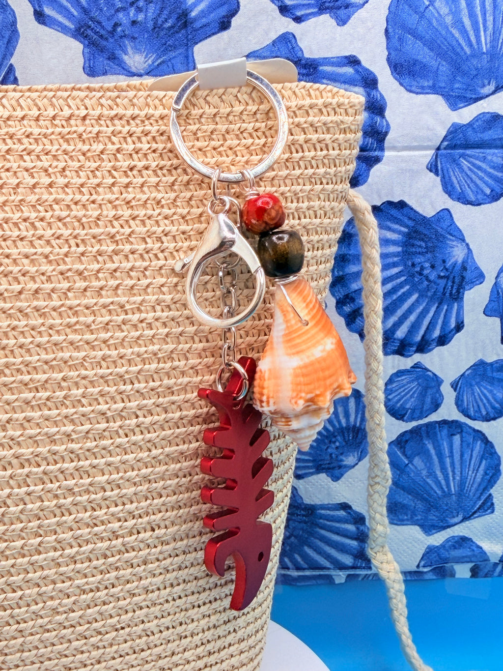 Florida conch shell red fishbone bottle opener keychain on woven straw bag showing red coral bead and dark wood bead detail
