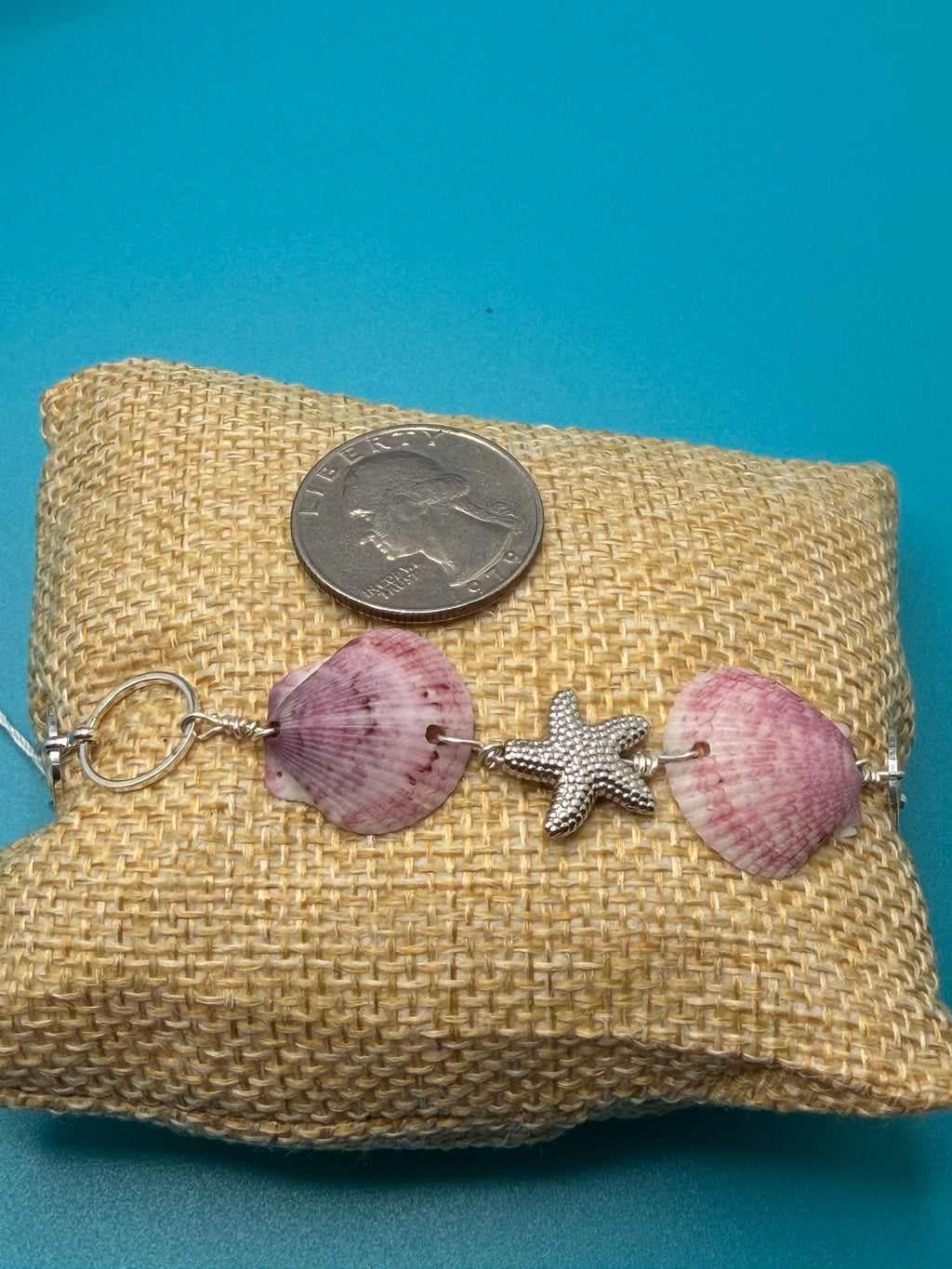 Purple calico scallop shell and starfish bracelet on burlap pillow with quarter for scale on blue background