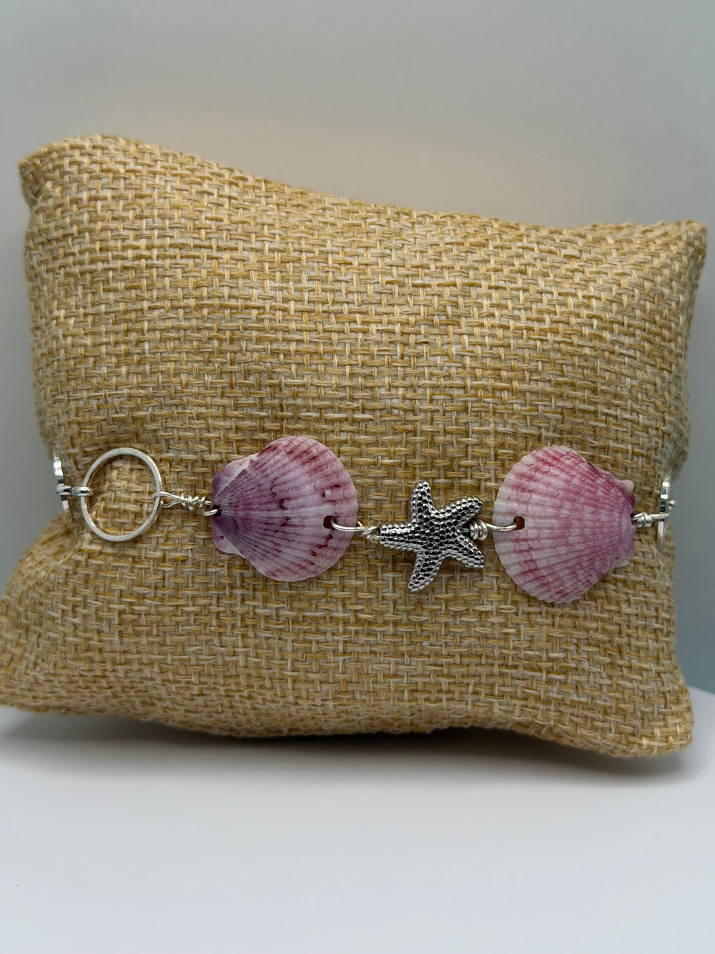 Purple calico scallop shell and starfish bracelet on burlap display pillow front view