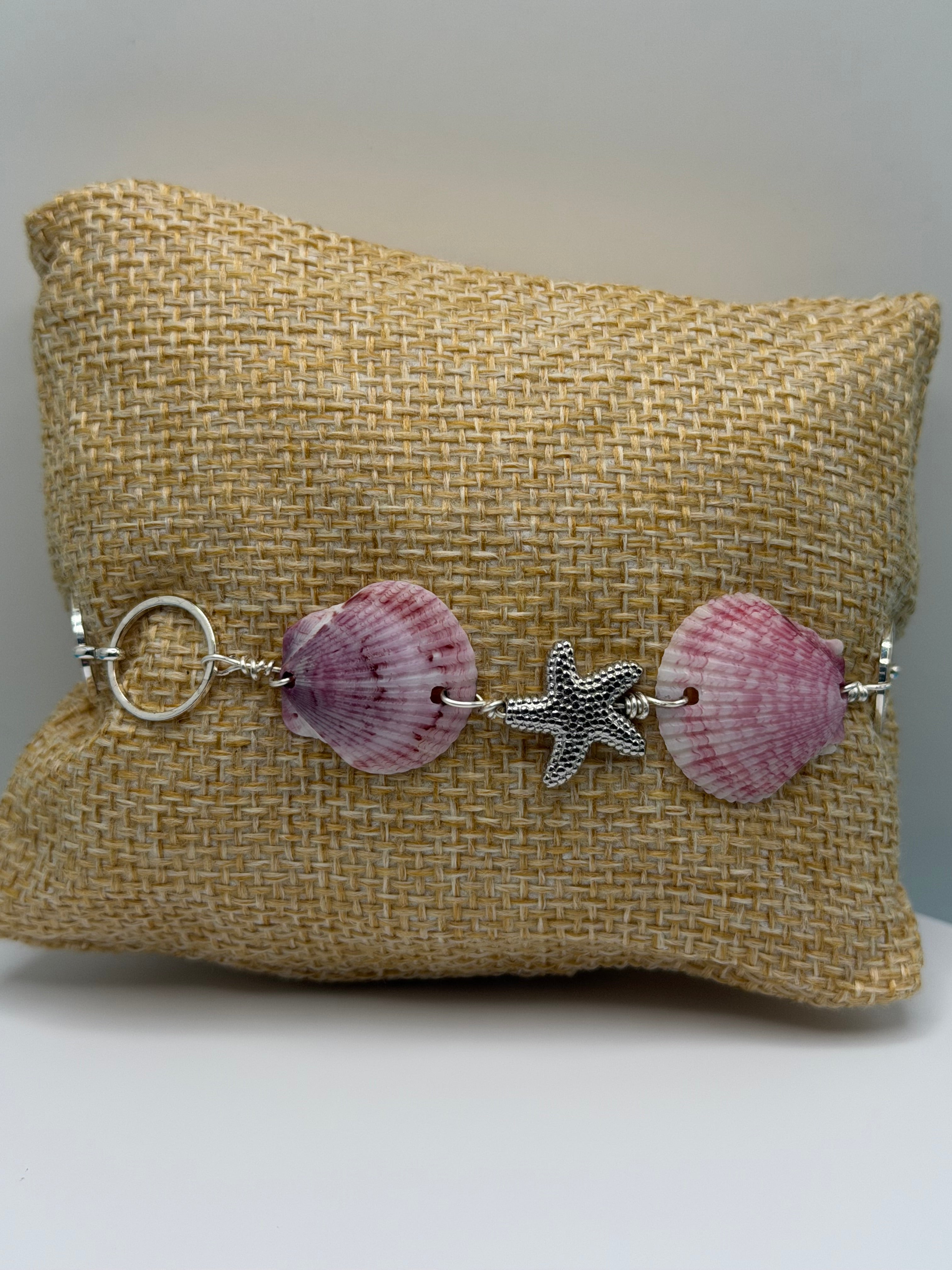 Purple calico scallop shell and starfish bracelet on burlap display pillow front view