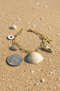 Ribbed venus clam shell charm bracelet on blue background with quarter for scale