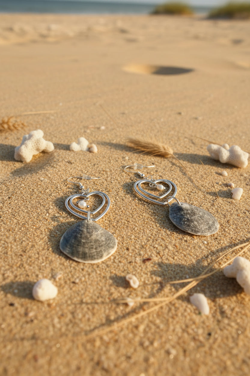 Pair of gray jingle shell double heart earrings on blue background with dime for scale overhead view