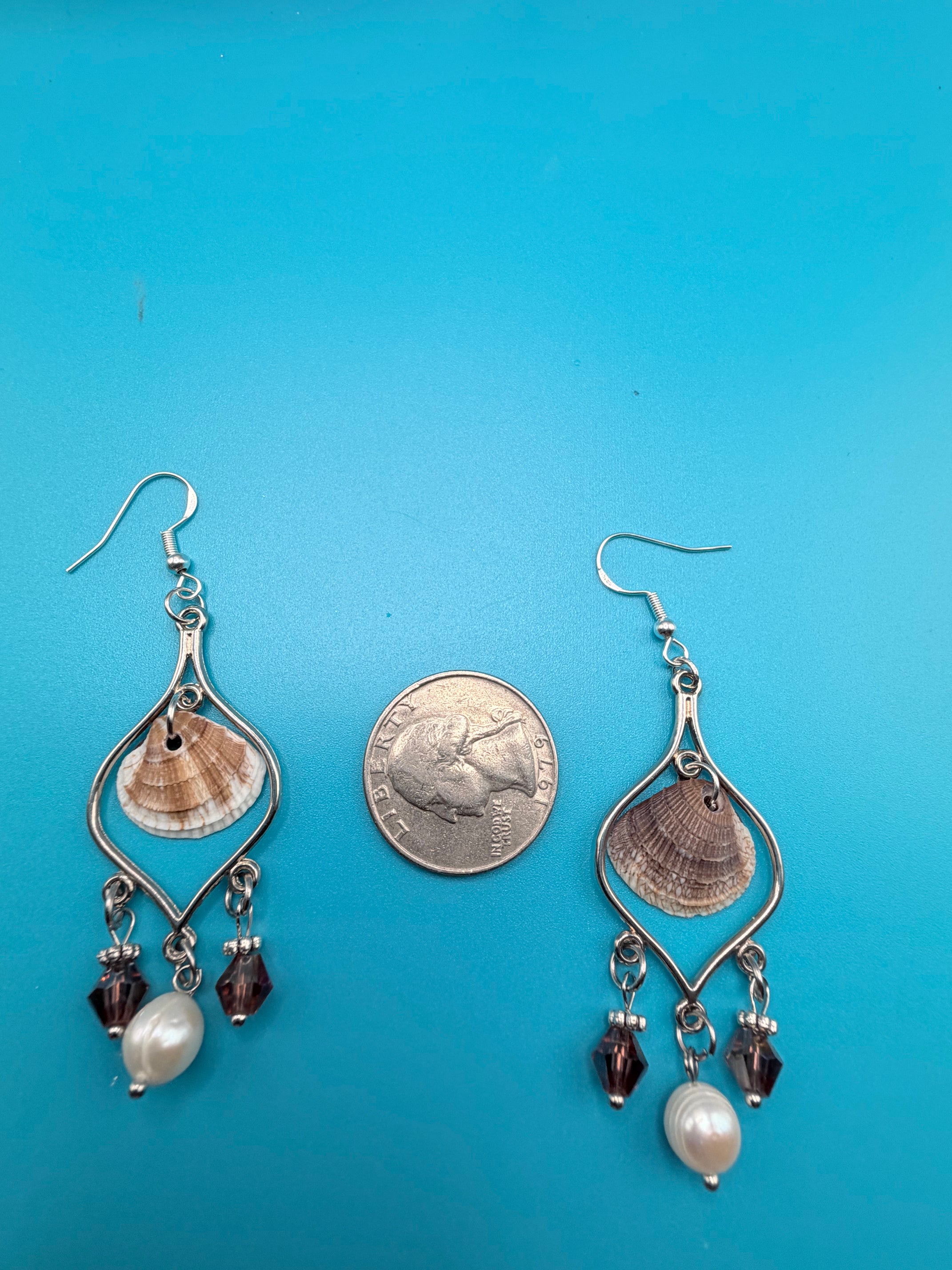 Single calico scallop shell chandelier earring on blue background with quarter for scale