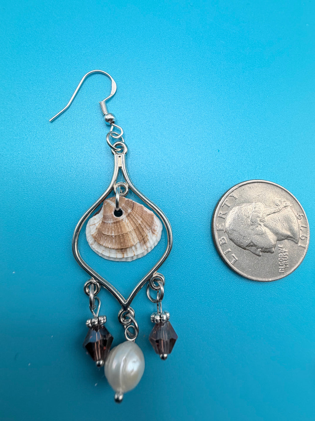 Pair of calico scallop shell chandelier earrings on blue background with dime for scale