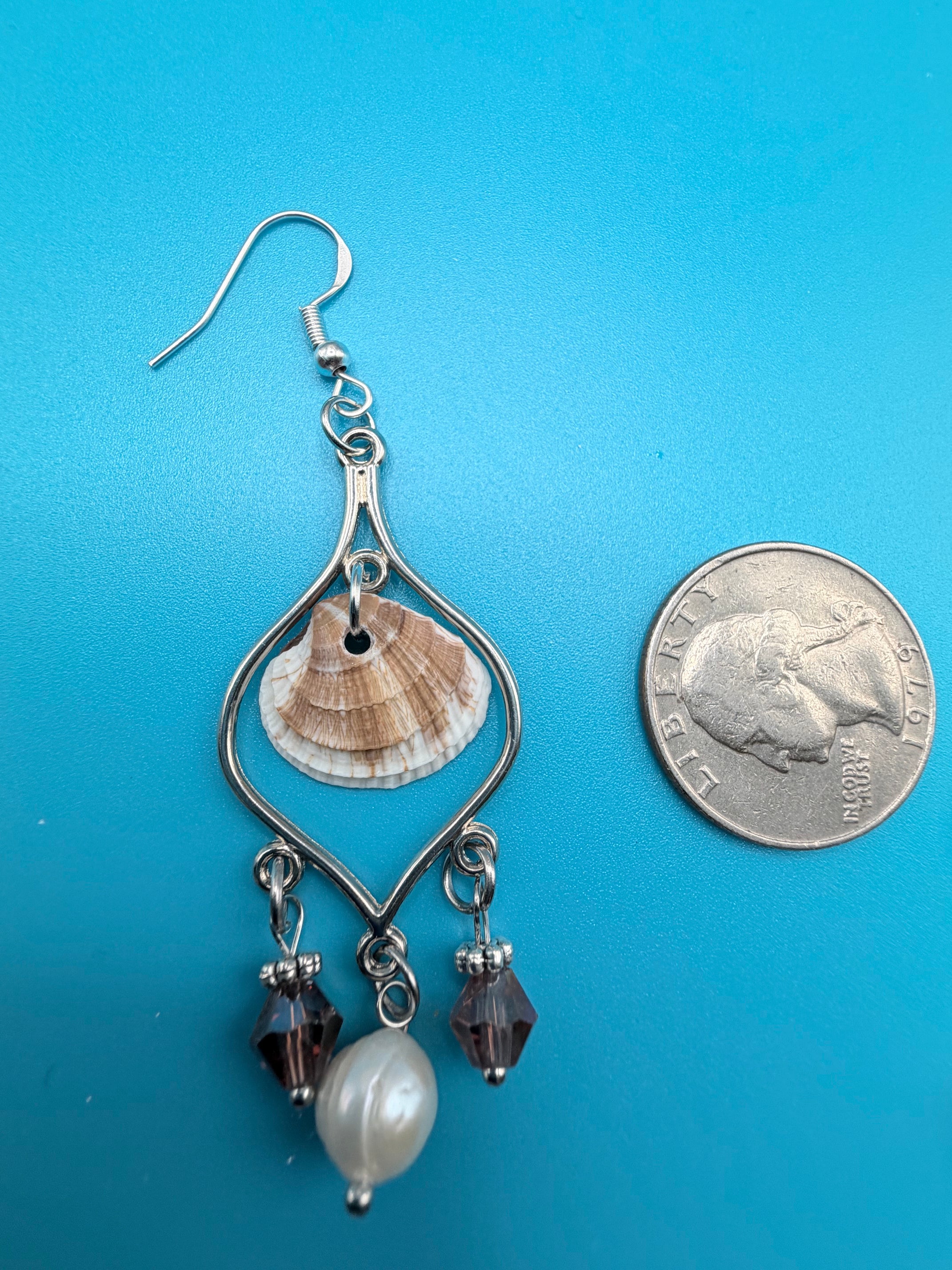 Pair of calico scallop shell chandelier earrings on blue background with dime for scale