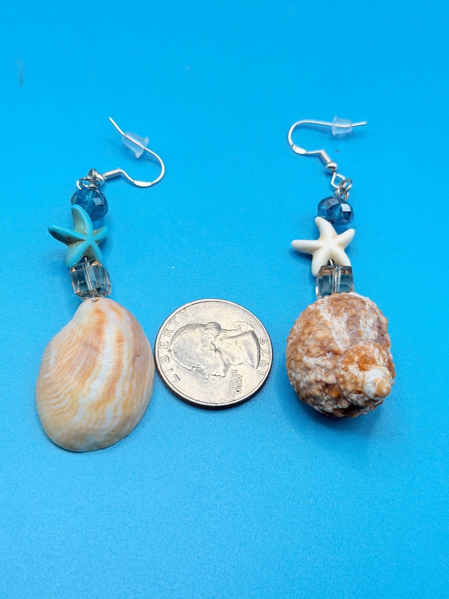 Mismatched turban and slipper shell earrings on display board with ruler showing drop length