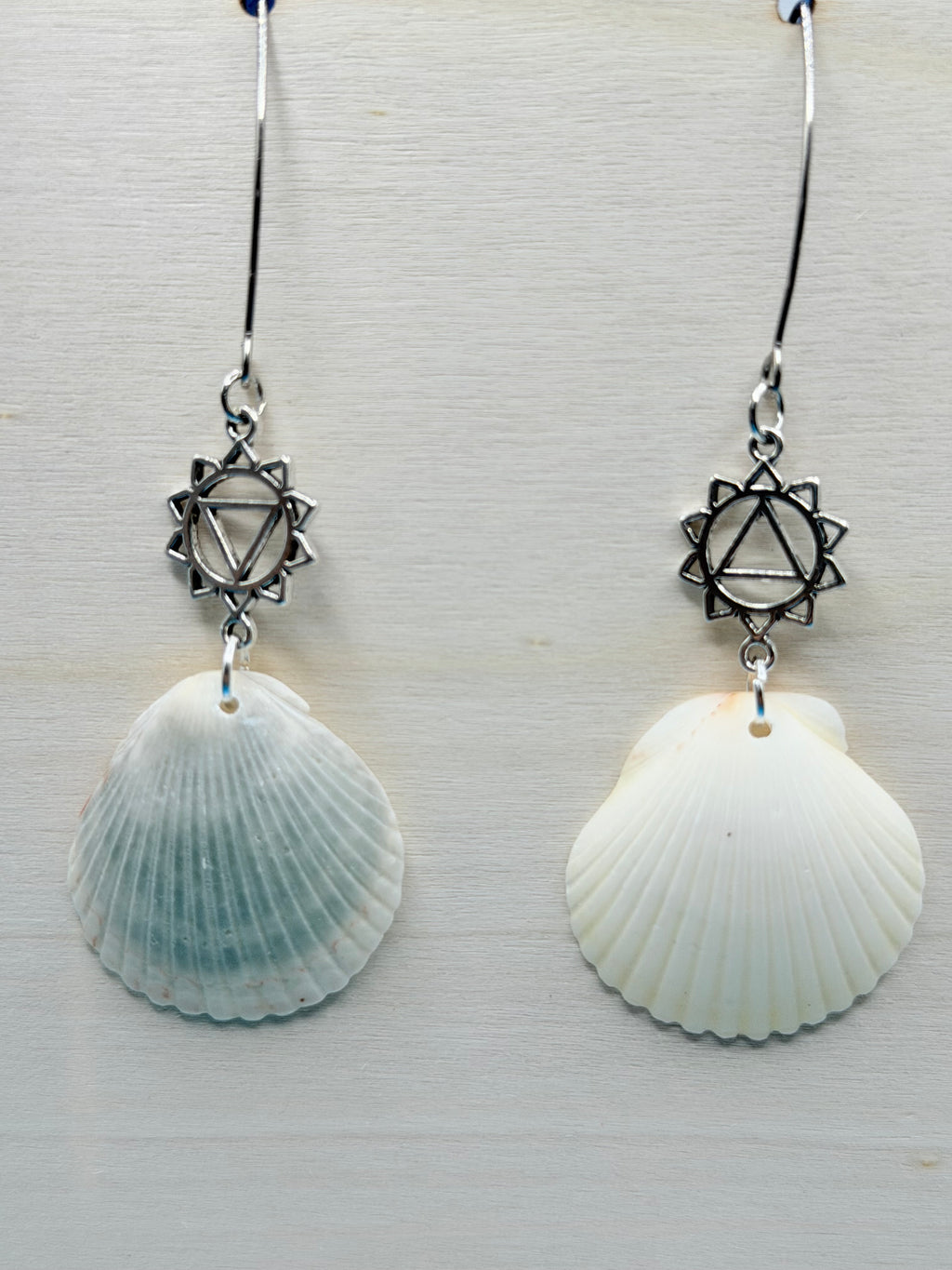 Close-up of silver chakra charm on scallop shell earring