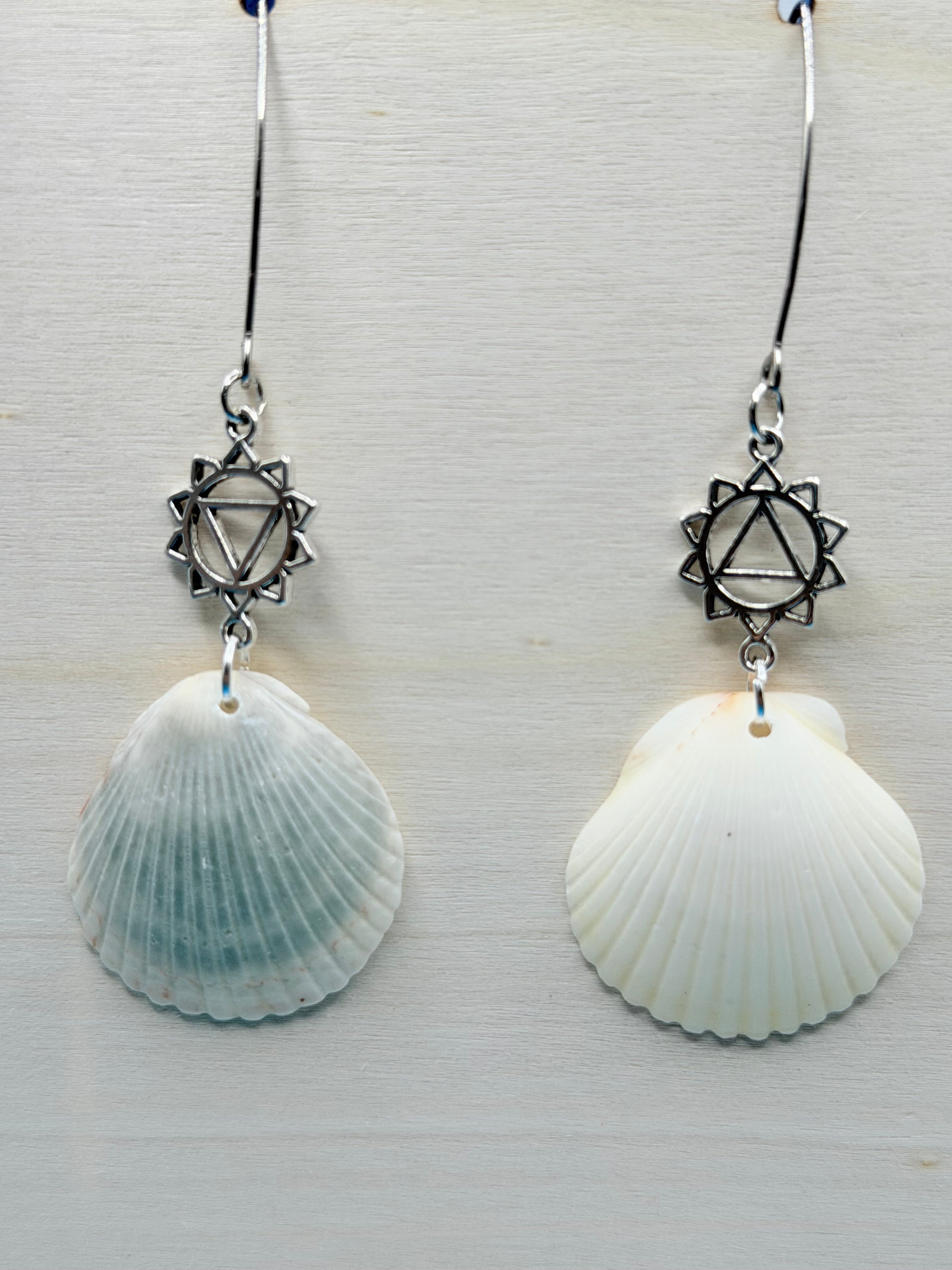 Close-up of silver chakra charm on scallop shell earring