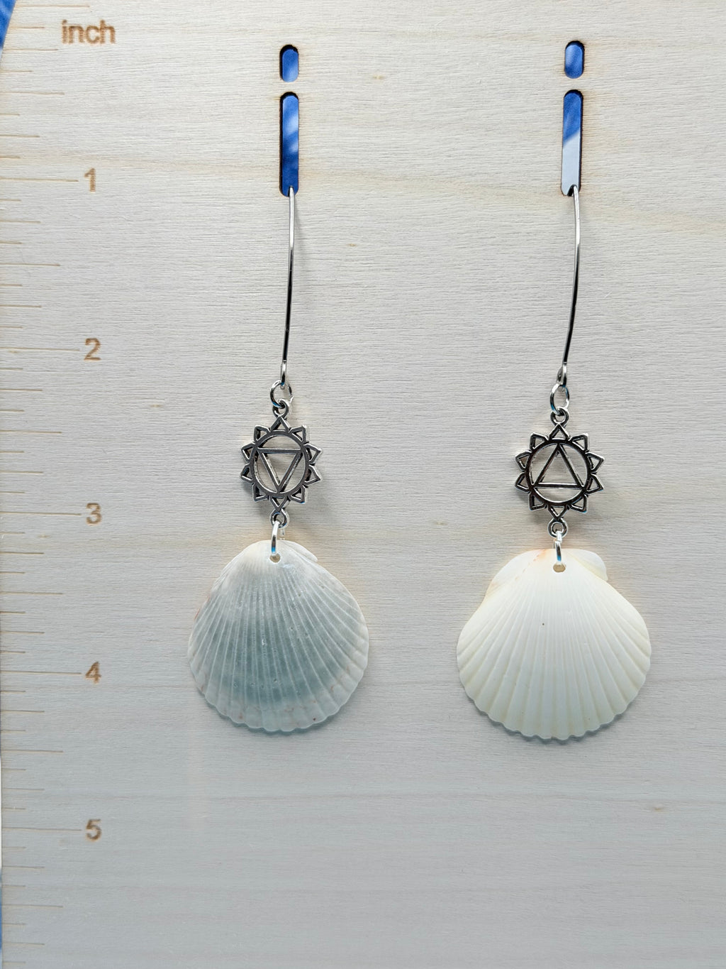 Single scallop shell chakra earring on blue background with quarter for scale