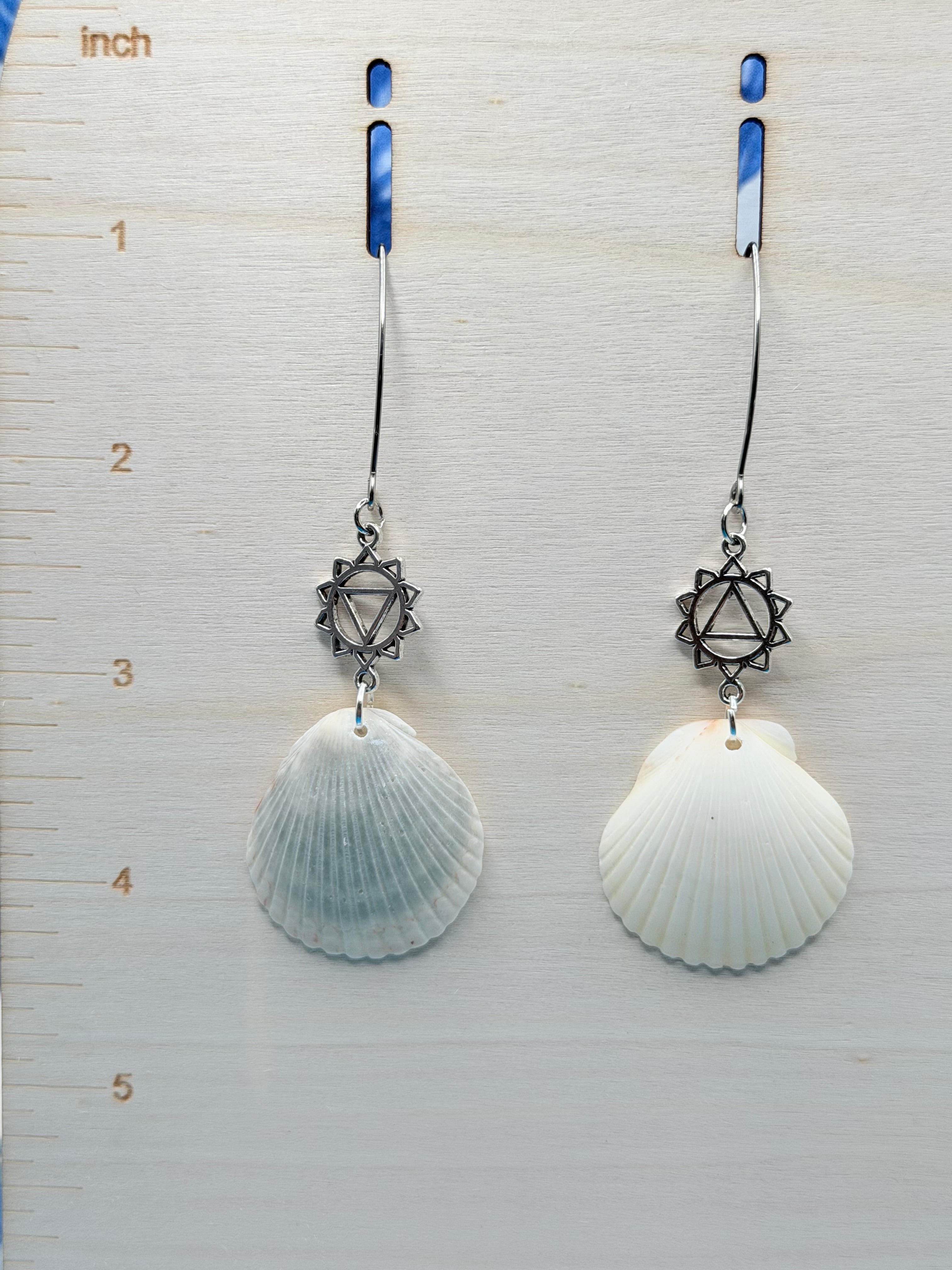 Single scallop shell chakra earring on blue background with quarter for scale