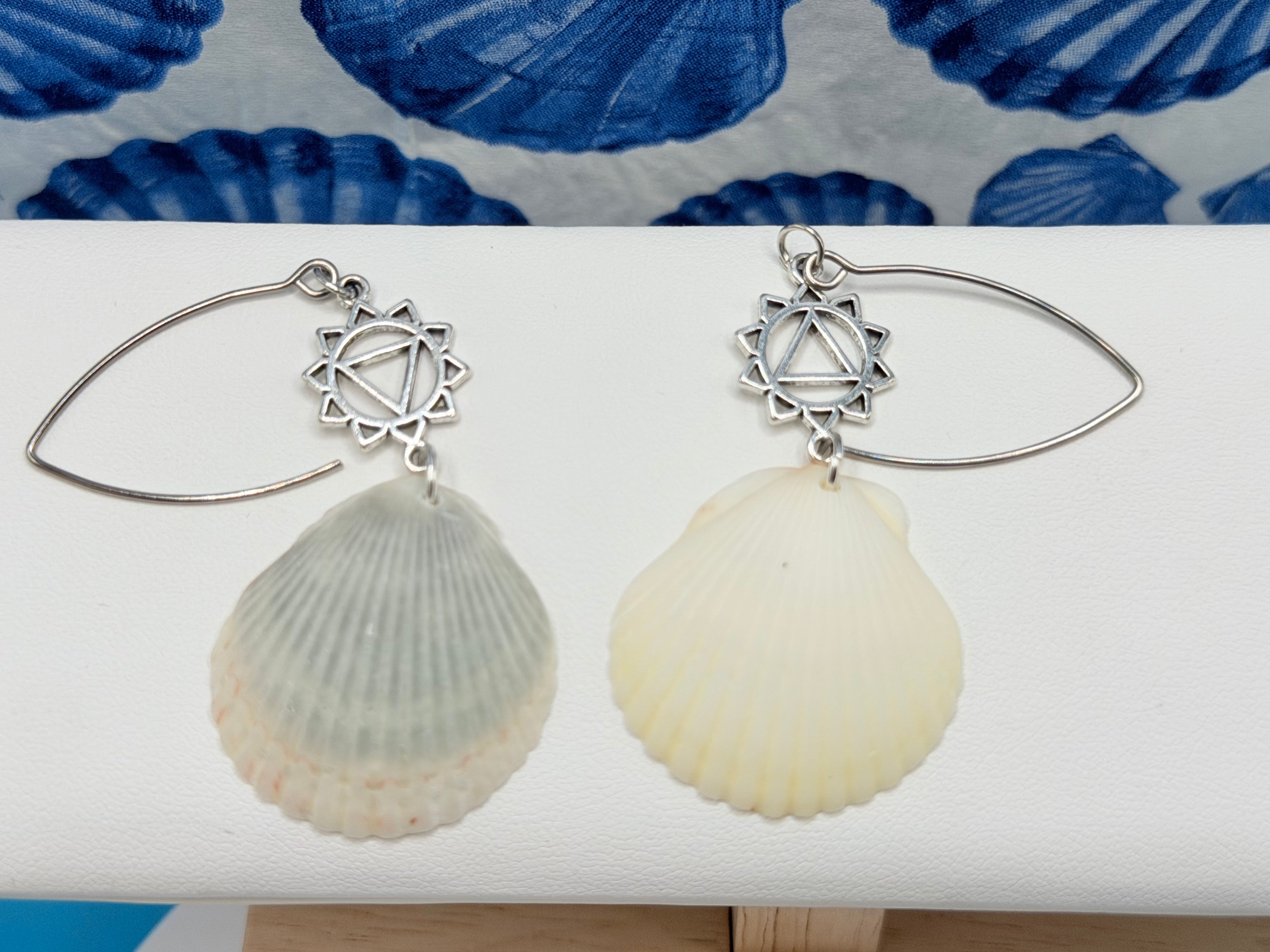 Pair of scallop shell chakra earrings on blue background showing both shells