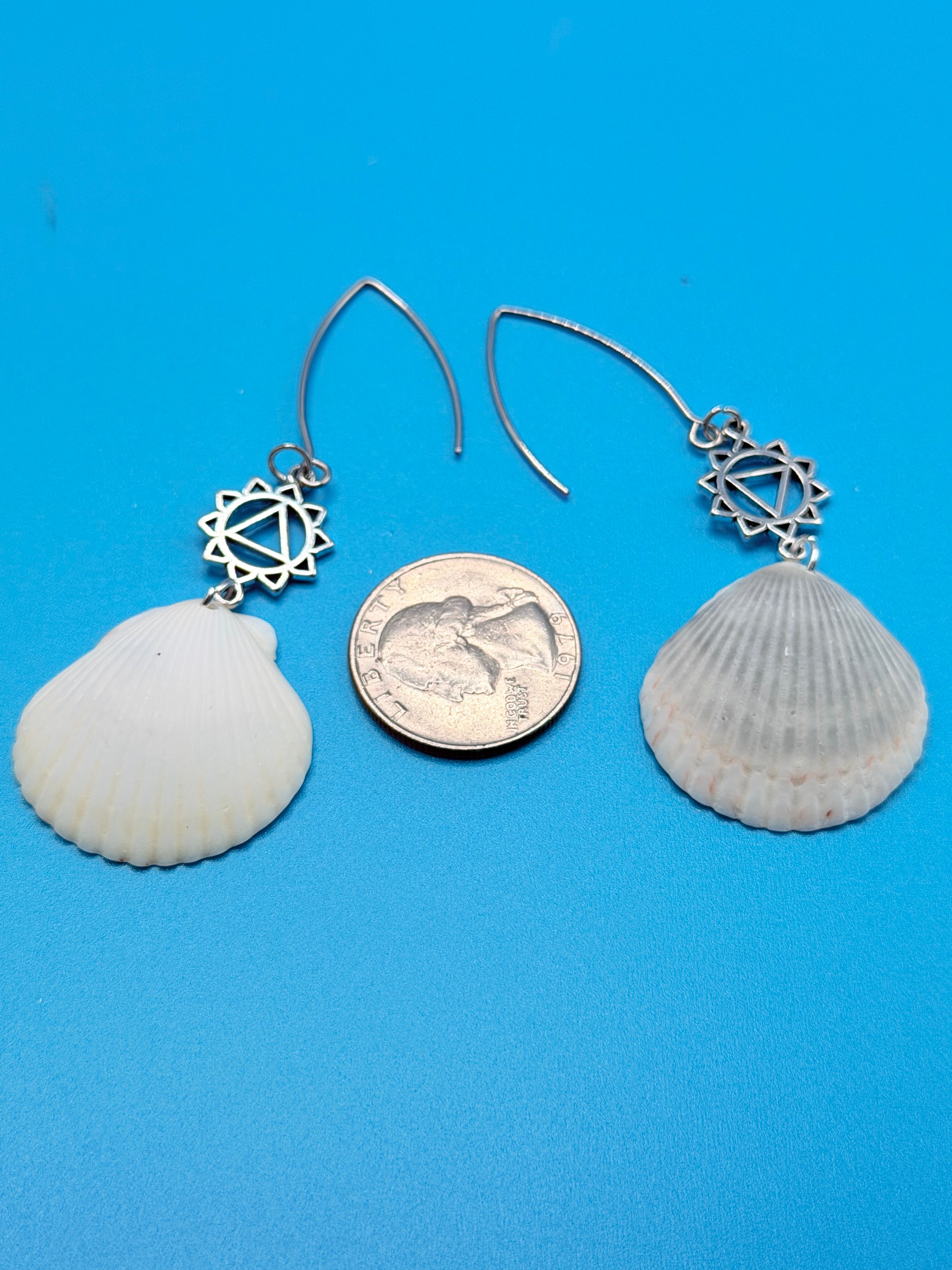 Pair of scallop shell chakra earrings on white display stand with shell backdrop