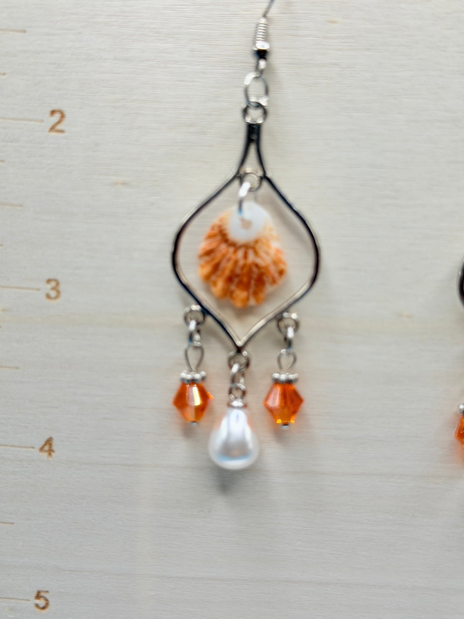 Pair of kitten paw shell chandelier earrings on white display stand with blue backdrop
