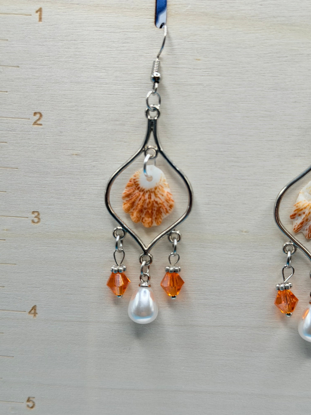Pair of kitten paw shell chandelier earrings with quarter for scale on blue background