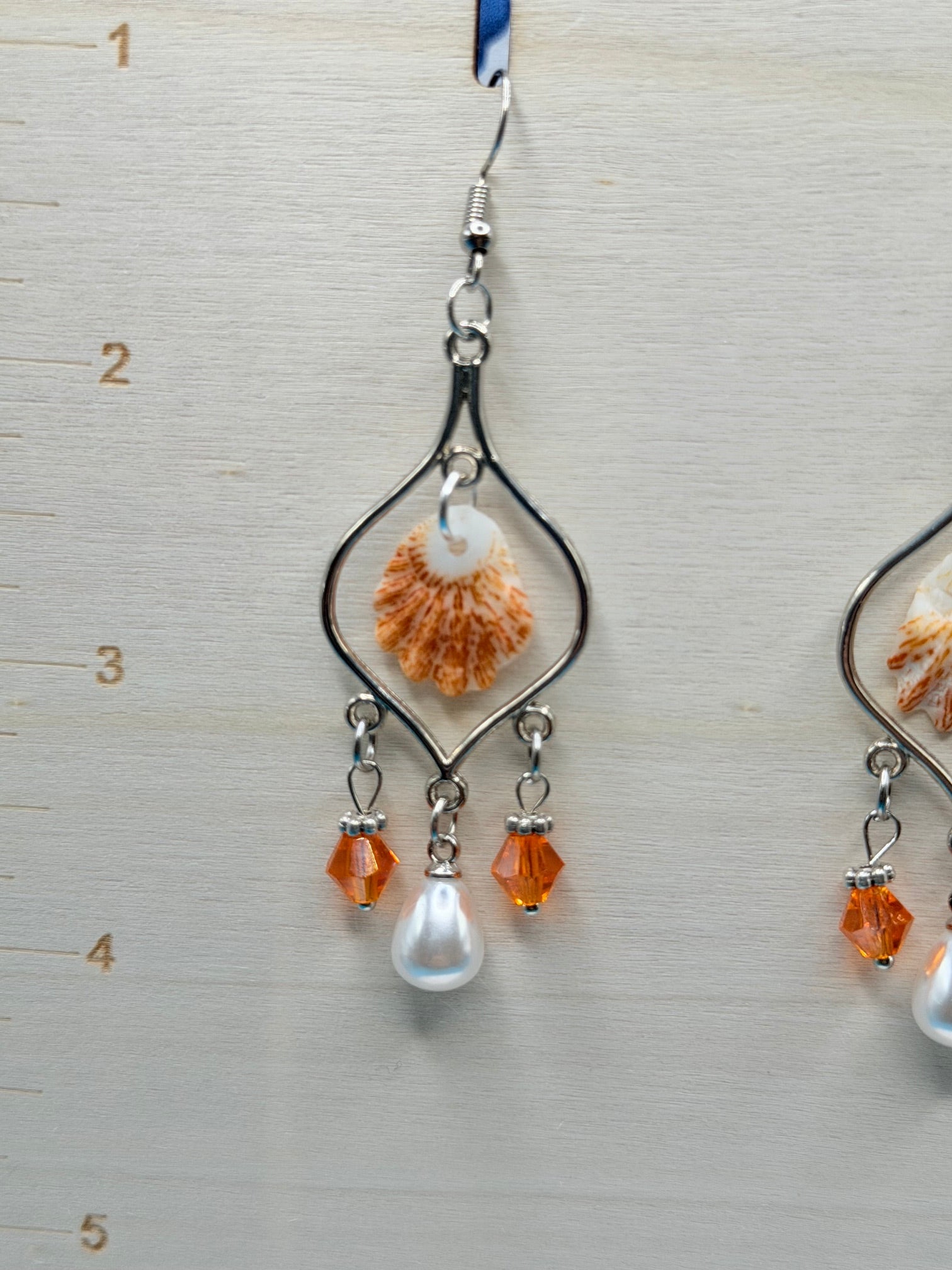 Pair of kitten paw shell chandelier earrings with quarter for scale on blue background