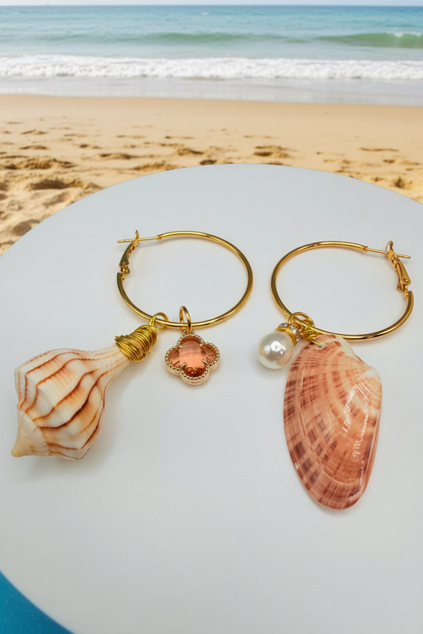 Mismatched shell hoop earrings on white surface showing both shells and clover charm
