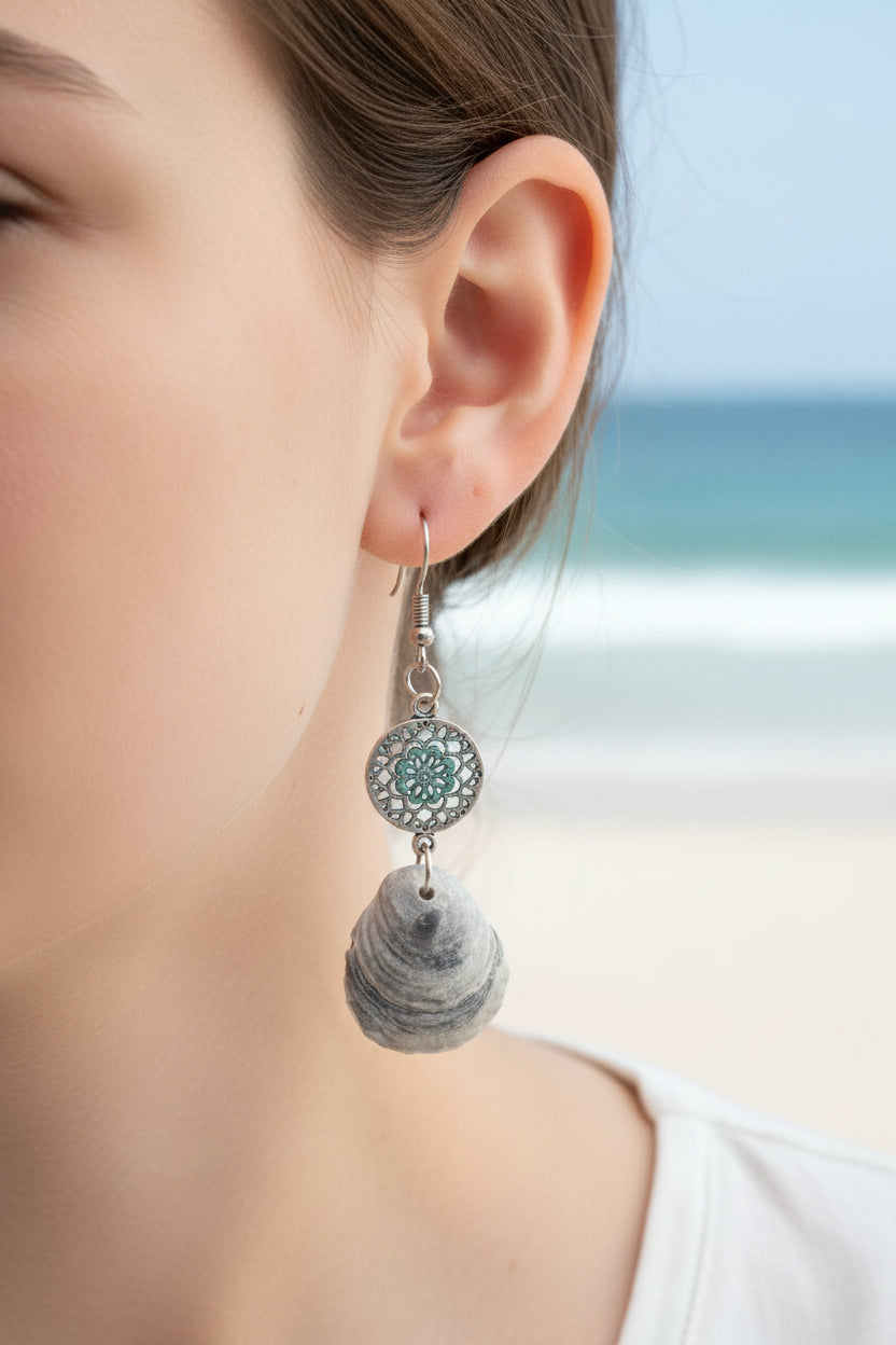 Pair of jingle shell earrings hanging on gold earring display stand with blue shell print background
