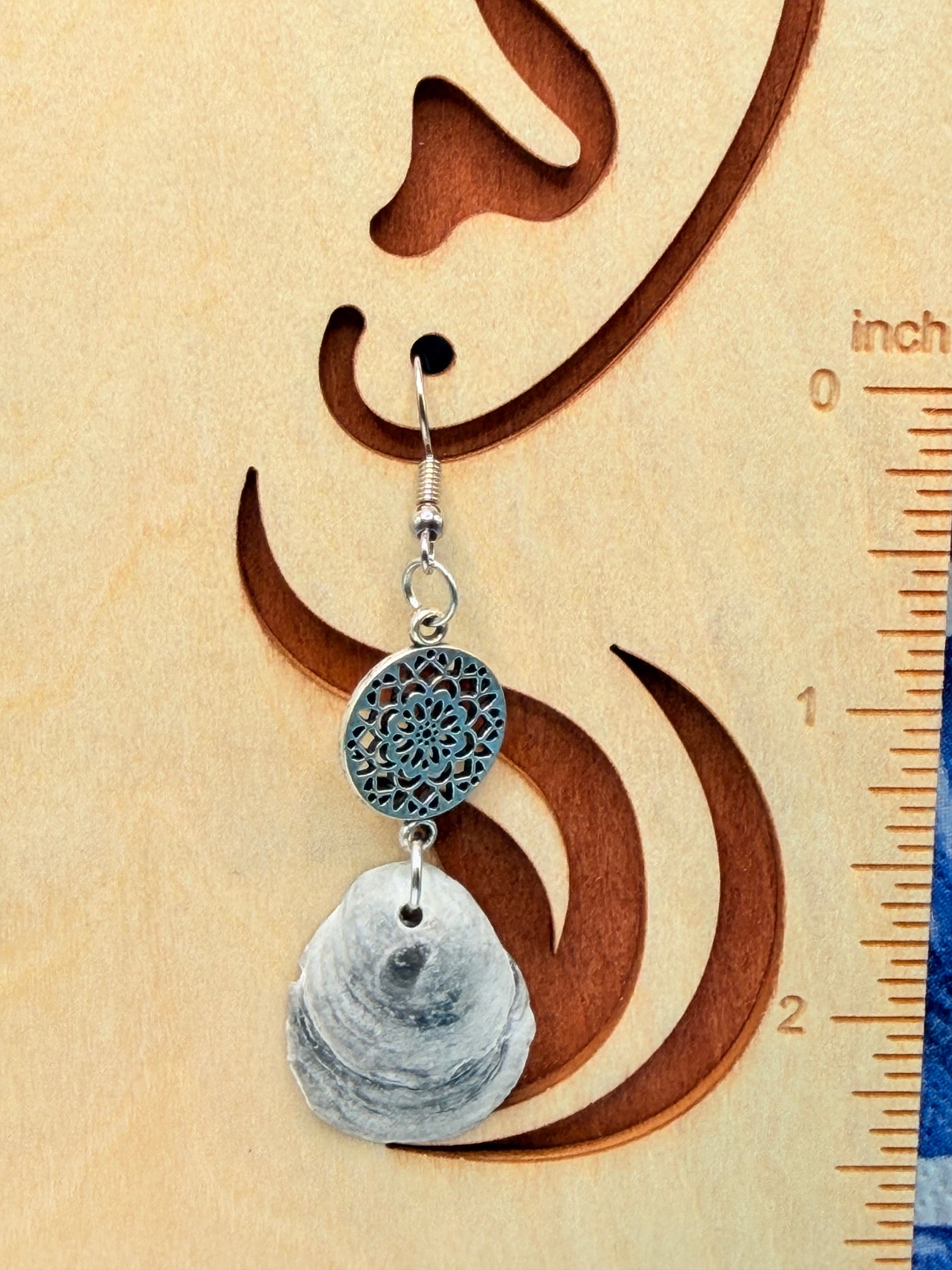 Close-up of single jingle shell earring with silver filigree mandala charm next to quarter