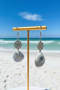 Pair of jingle shell earrings with silver filigree mandala charm next to quarter for size reference