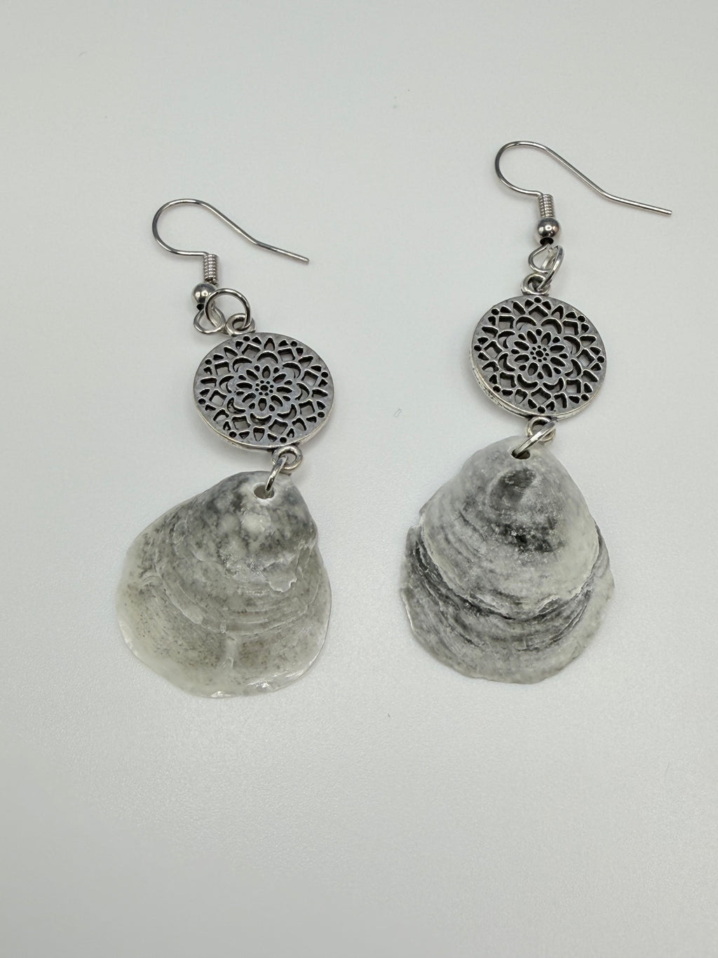 Jingle shell earrings close-up showing layered shell texture and silver mandala charm