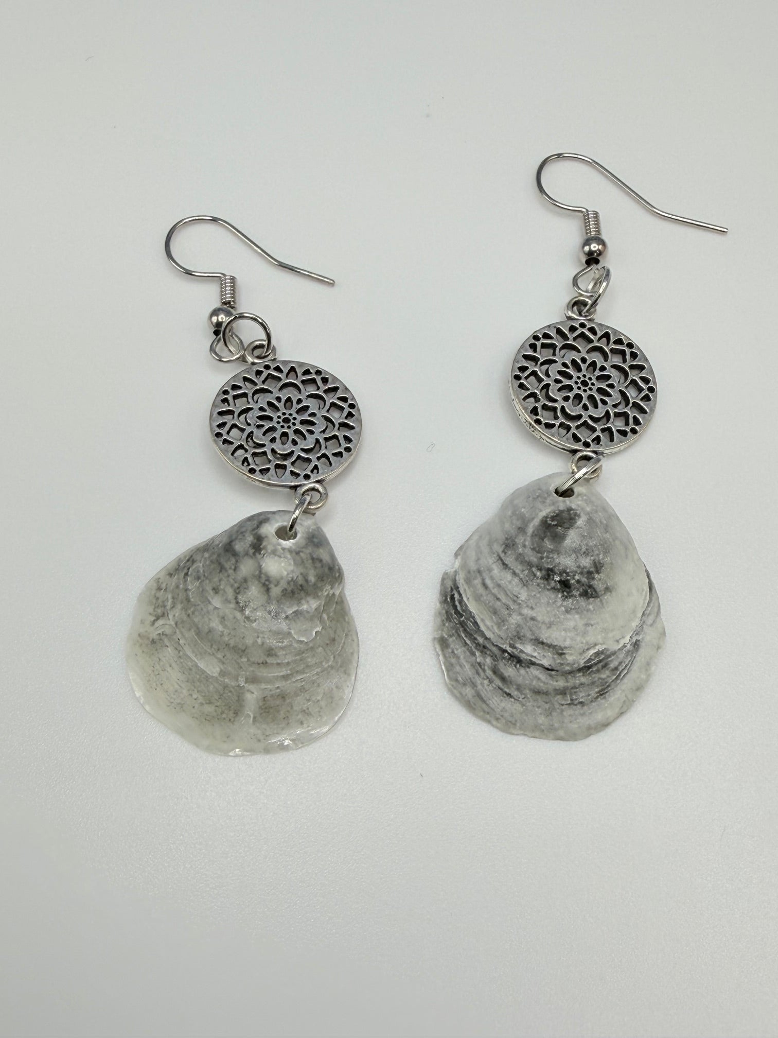 Jingle shell earrings close-up showing layered shell texture and silver mandala charm