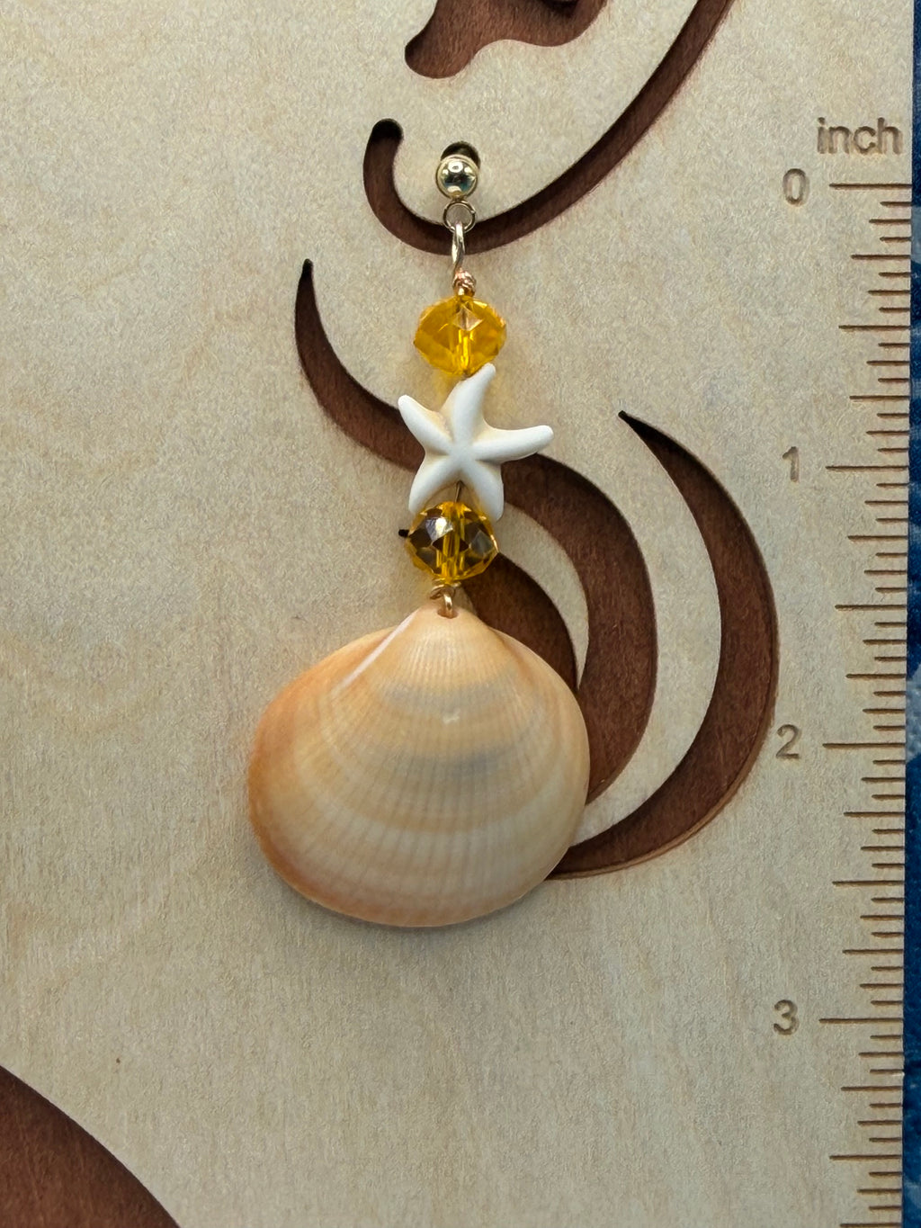 Single golden cockle shell earring on white display stand showing full drop and shell detail